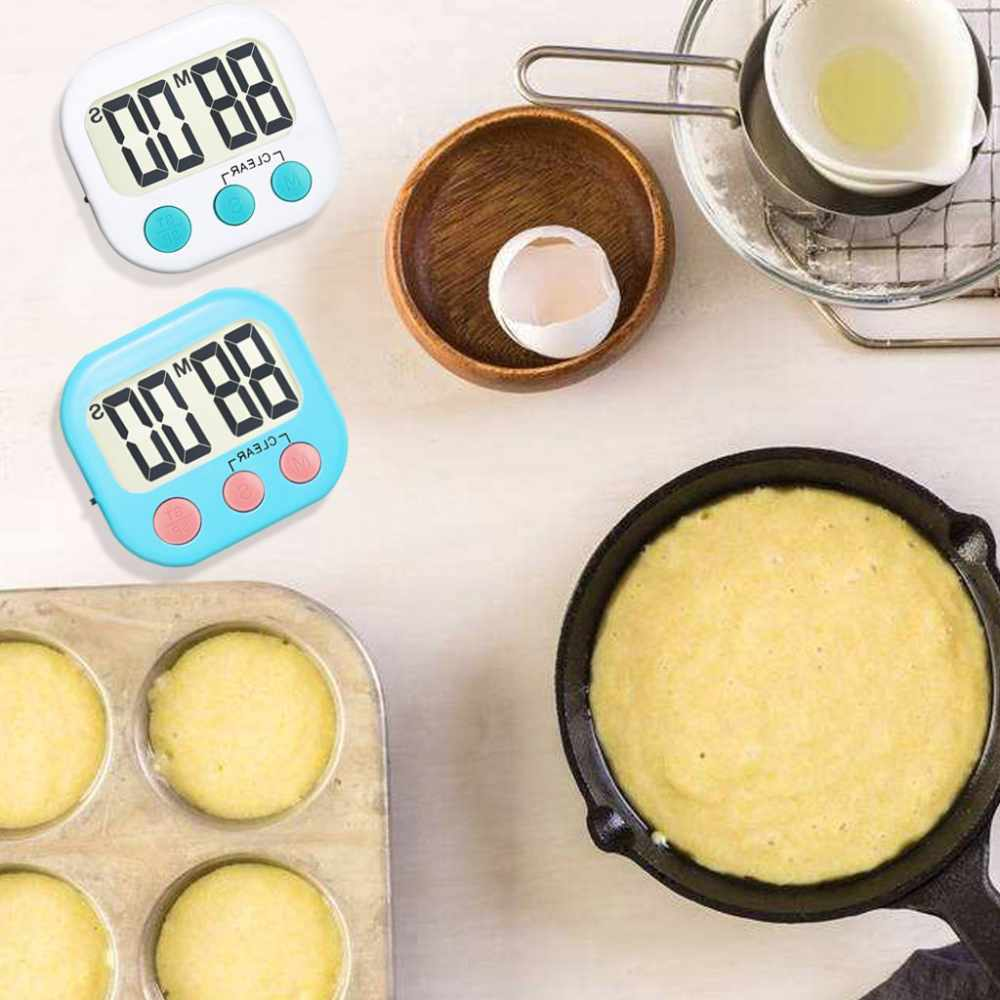 Backszene mit Timern, Teig und Zutaten. Zwei Timer, einer weiß, einer blau. Teig in der Pfanne und Muffins. Ei und Öl in Schalen.