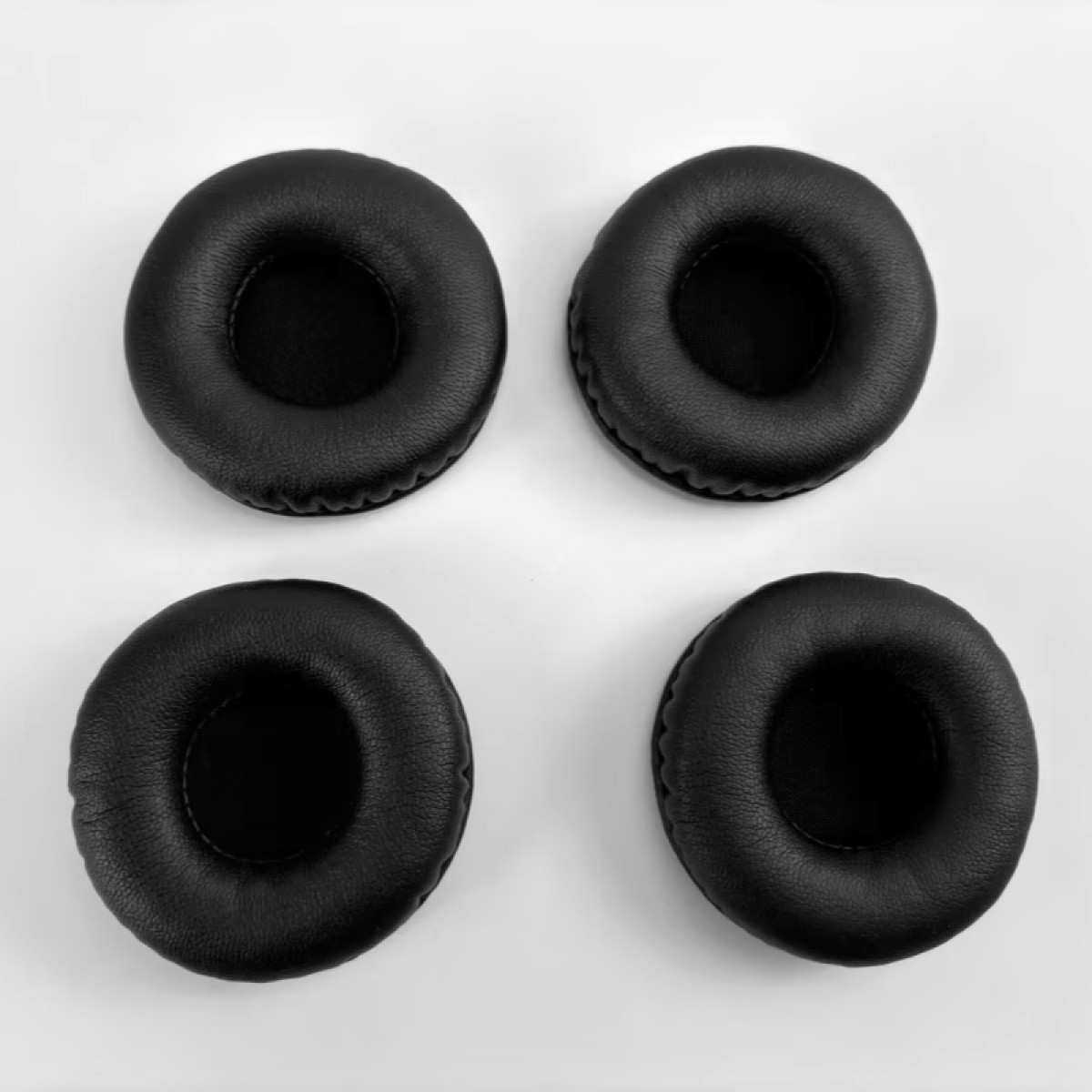 Cztery czarne nauszniki do słuchawek ułożone w kwadrat na białym tle. Każdy nausznik jest okrągły z centralnym otworem.