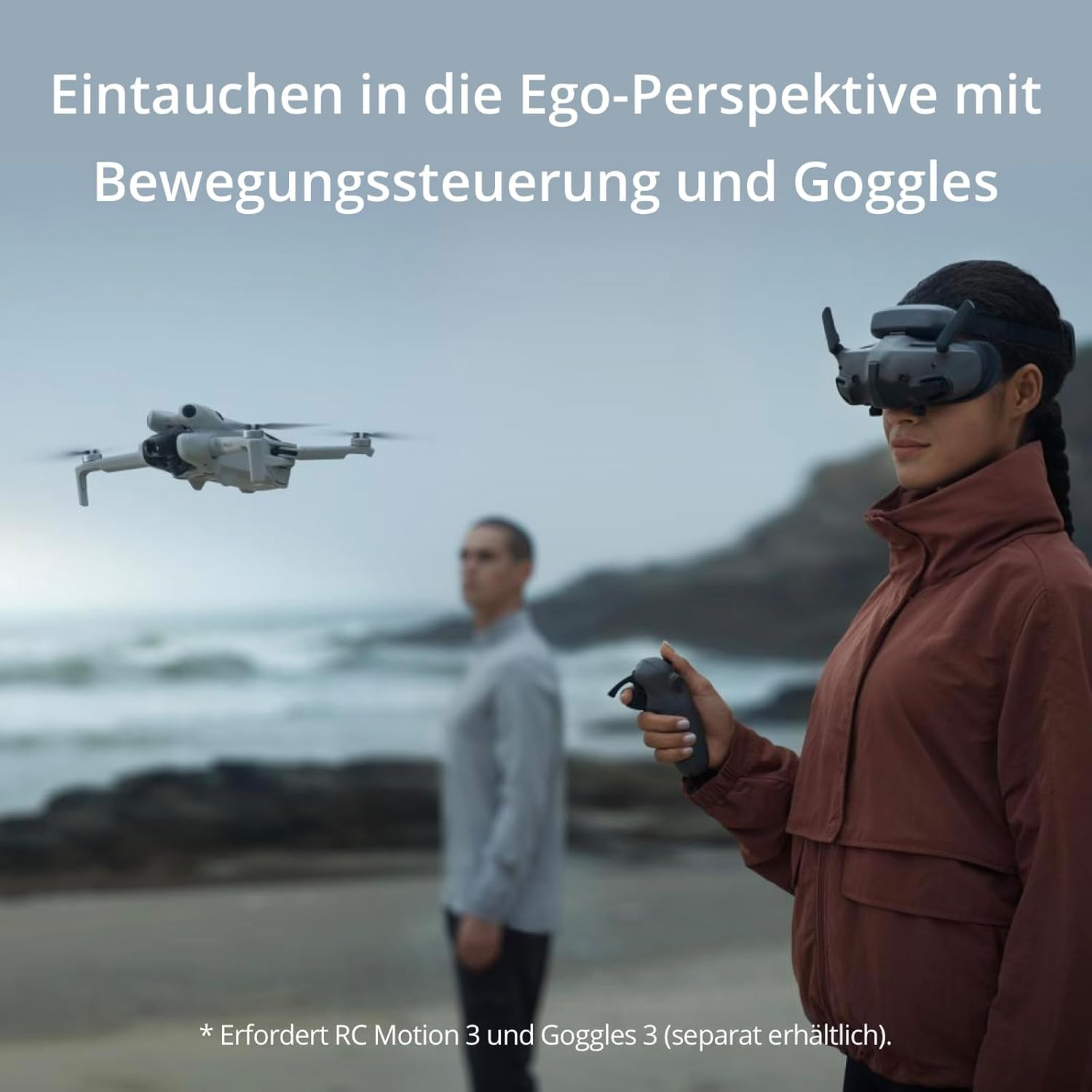 Eine Frau trägt eine VR-Brille und hält einen Controller. Eine Drohne fliegt in der Luft. Ein Mann steht im Hintergrund. Strandszene.