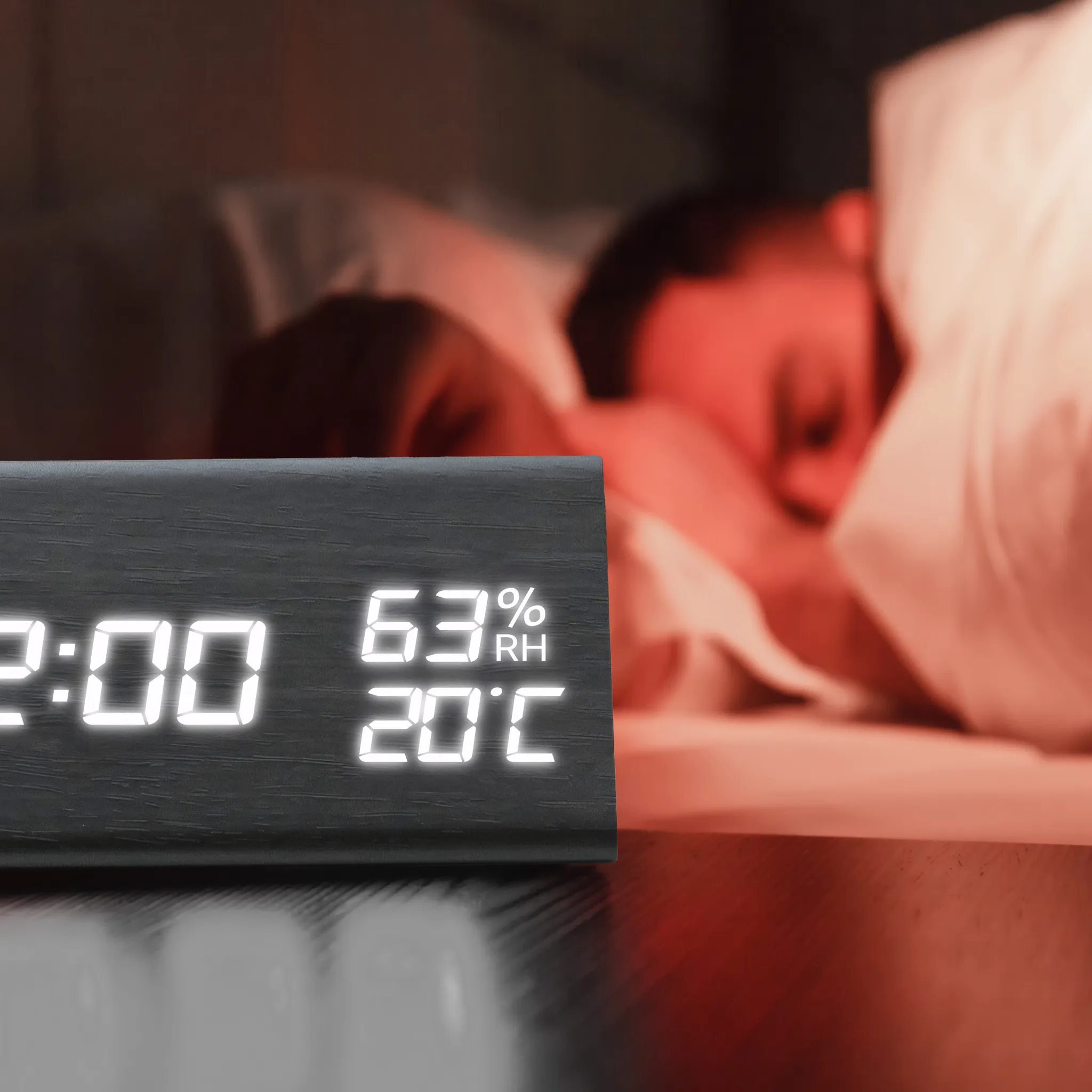 Eine Digitaluhr zeigt 2:00 Uhr, 63 % Luftfeuchtigkeit und 20 °C an. Im Hintergrund schläft eine Person mit einem weißen Kissen.