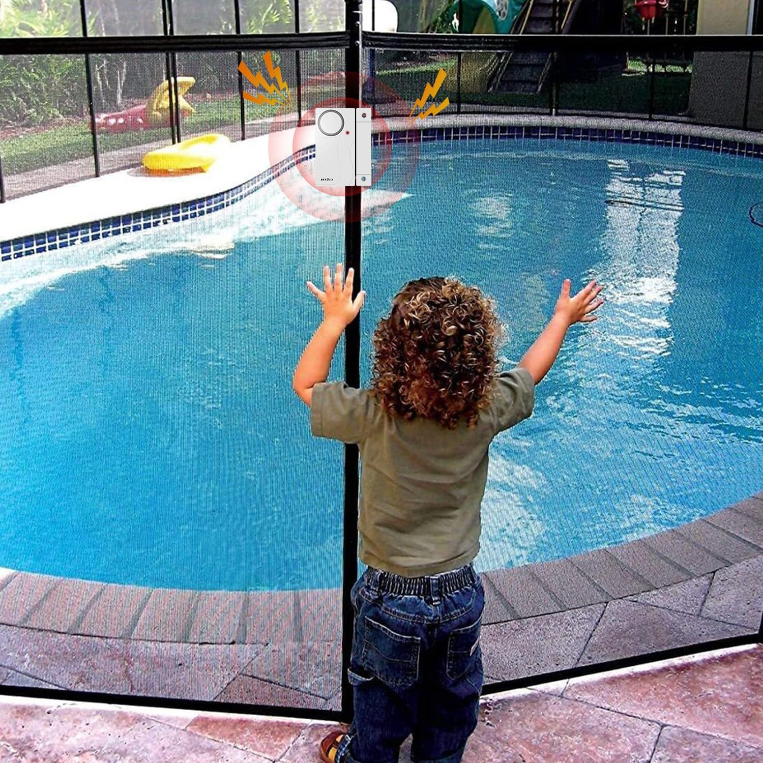 Ein Kind mit lockigem Haar steht in der Nähe eines Poolzauns. Das Kind hebt die Arme. Ein Poolalarm ist am Zaun befestigt.
