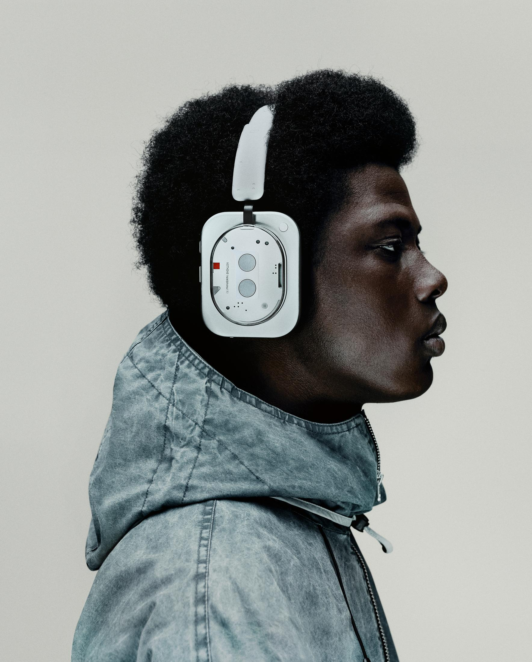 Mężczyzna w białych słuchawkach i niebieskiej kurtce. Mężczyzna patrzy w prawo. Tło jest gładkie.