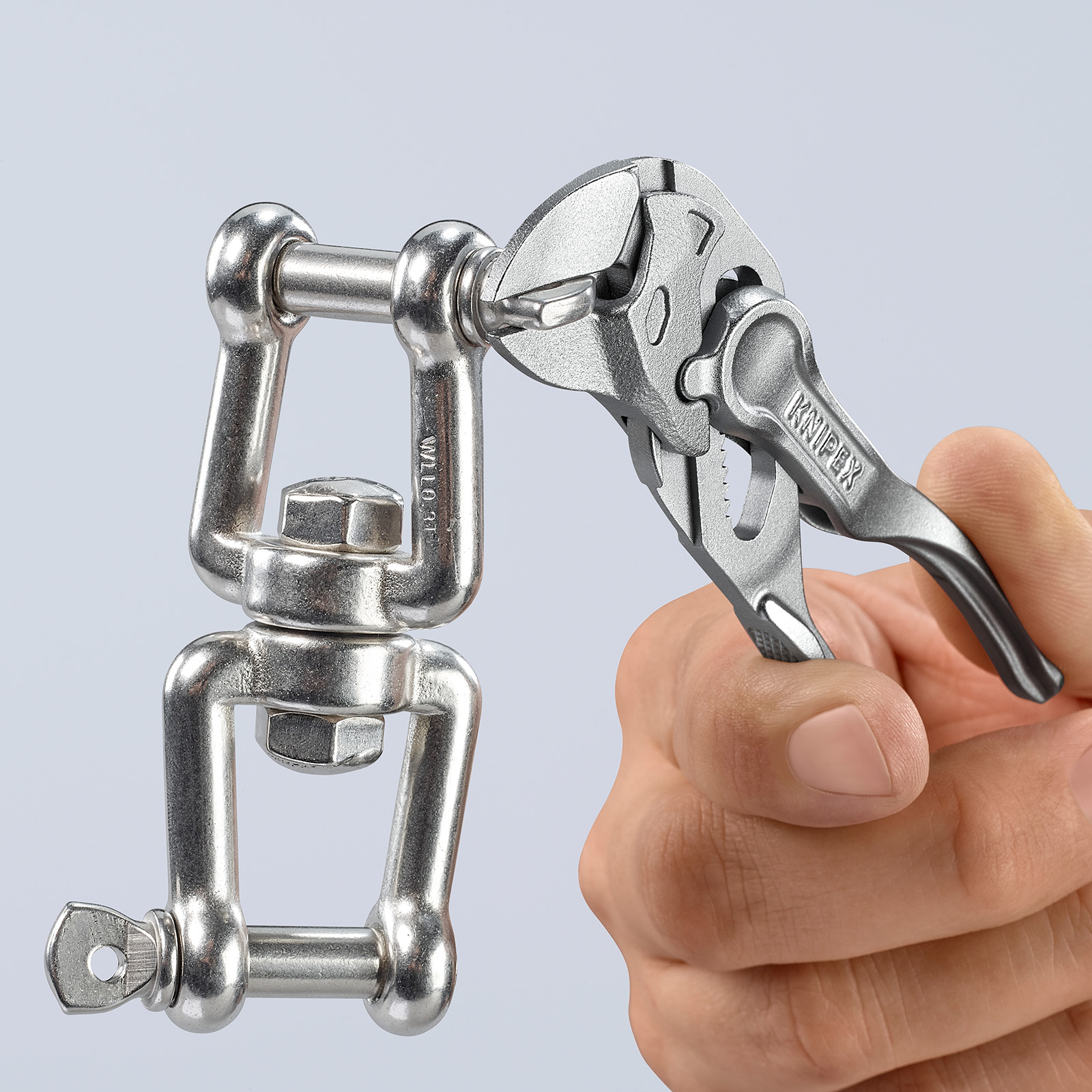 Eine Hand hält einen Schraubenschlüssel und greift einen Metallwirbelverbinder. Der Schraubenschlüssel ist mit 'KNIPEX' beschriftet. Der Hintergrund ist hellgrau.