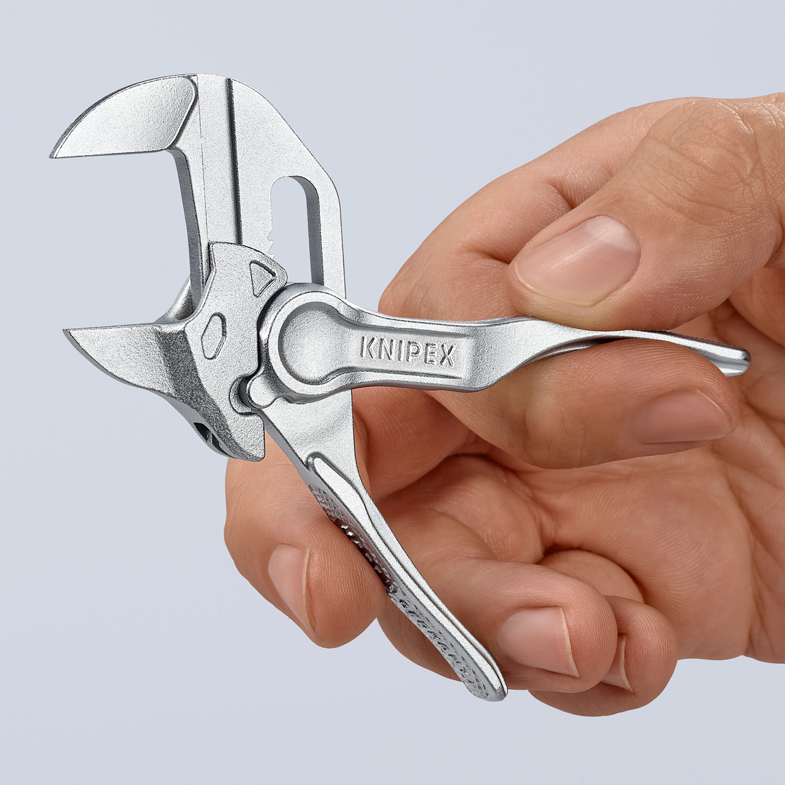 Eine Hand hält einen silbernen Knipex-Zangen-Schlüssel. Das Werkzeug ist geöffnet, der Markenname ist auf dem Griff sichtbar. Der Hintergrund ist schlicht.