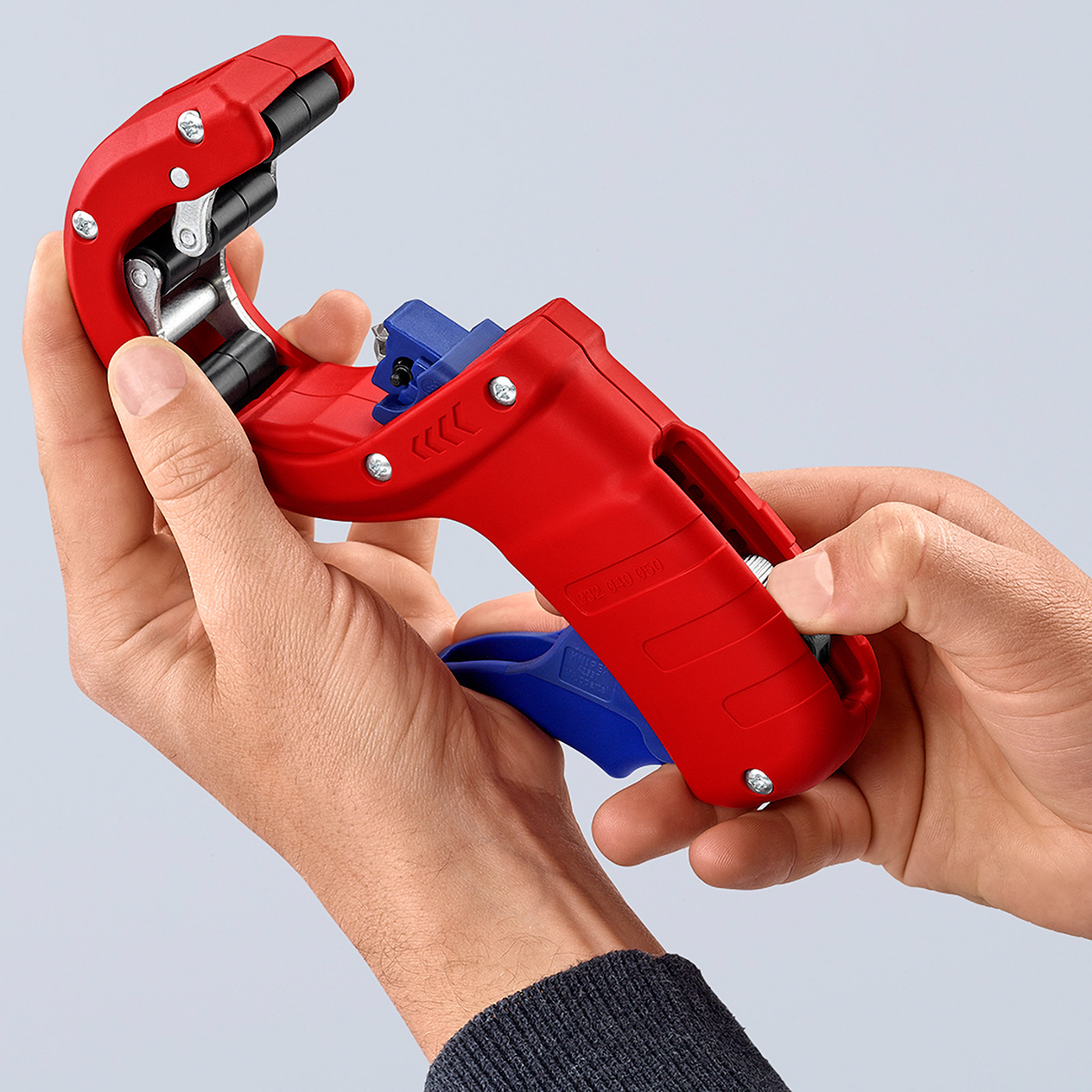 Mains tenant un outil de dénudage rouge et bleu. L'outil est utilisé, avec un fil inséré.