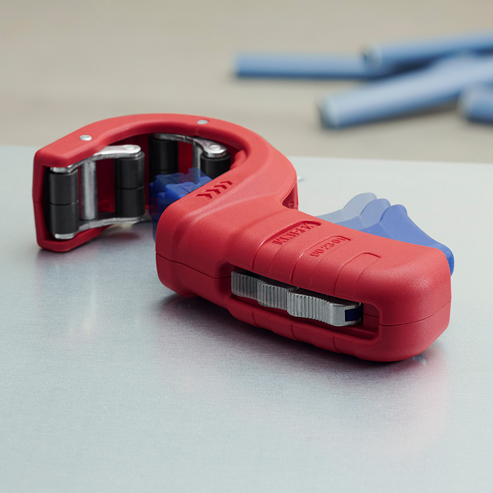 Un coupe-tube rouge et bleu sur une surface métallique. Tuyaux bleus flous en arrière-plan.