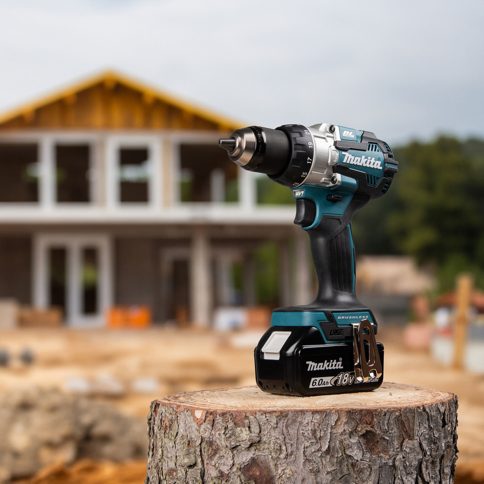 Ein Akku-Bohrschrauber von Makita steht auf einem Baumstumpf, im Hintergrund ein Haus im Bau.