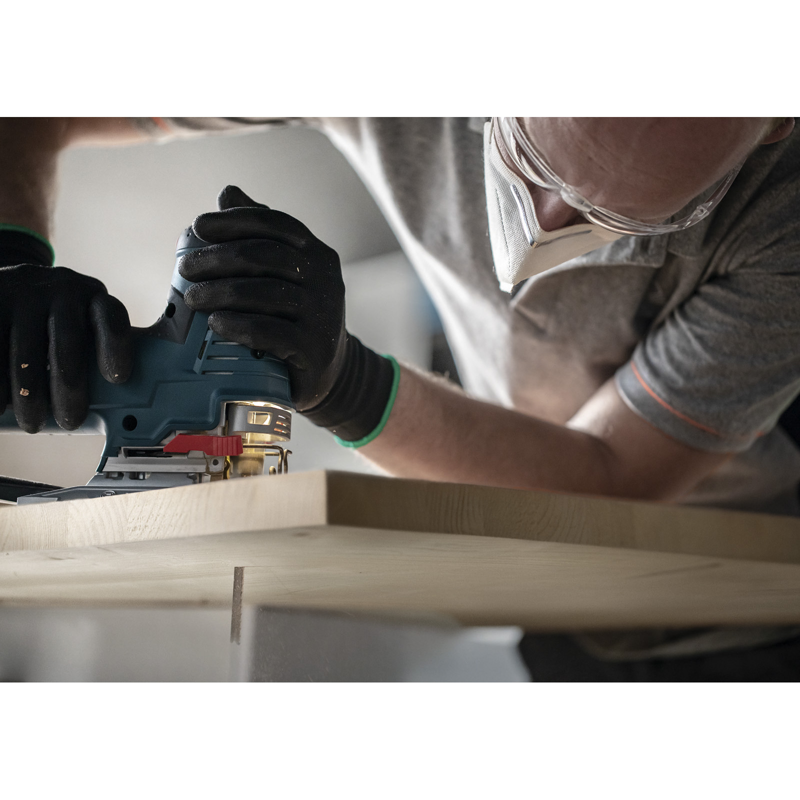 Osoba używa szlifierki na drewnianej powierzchni. Nosi okulary ochronne i rękawice, skupiając się na obróbce drewna.