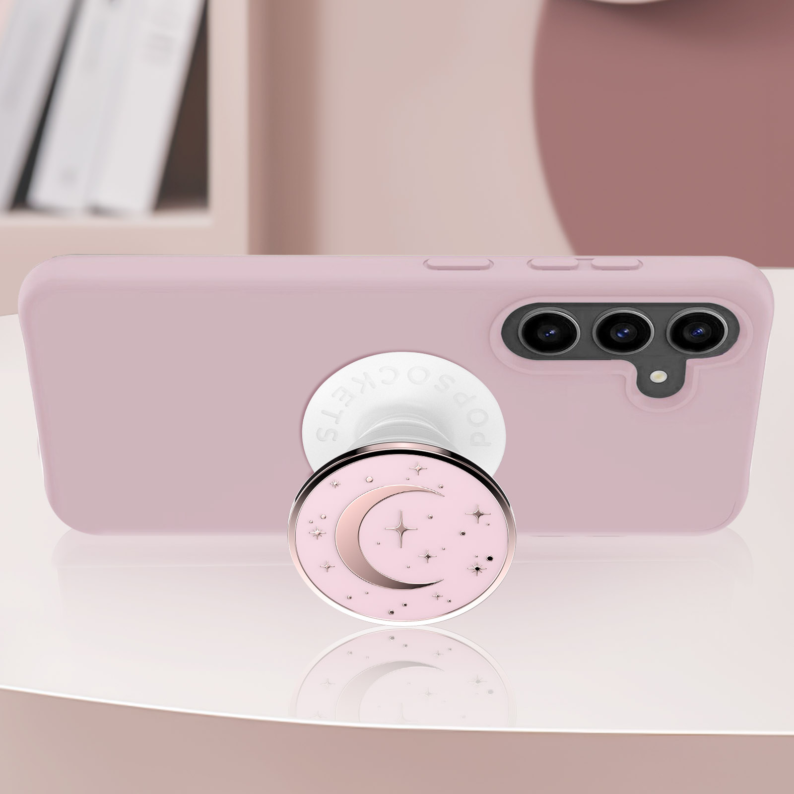 Ein rosa Telefon mit einem Mond- und Stern-PopSocket. Das Telefon liegt auf einem Tisch. Der Hintergrund ist ein verschwommenes Rosa.