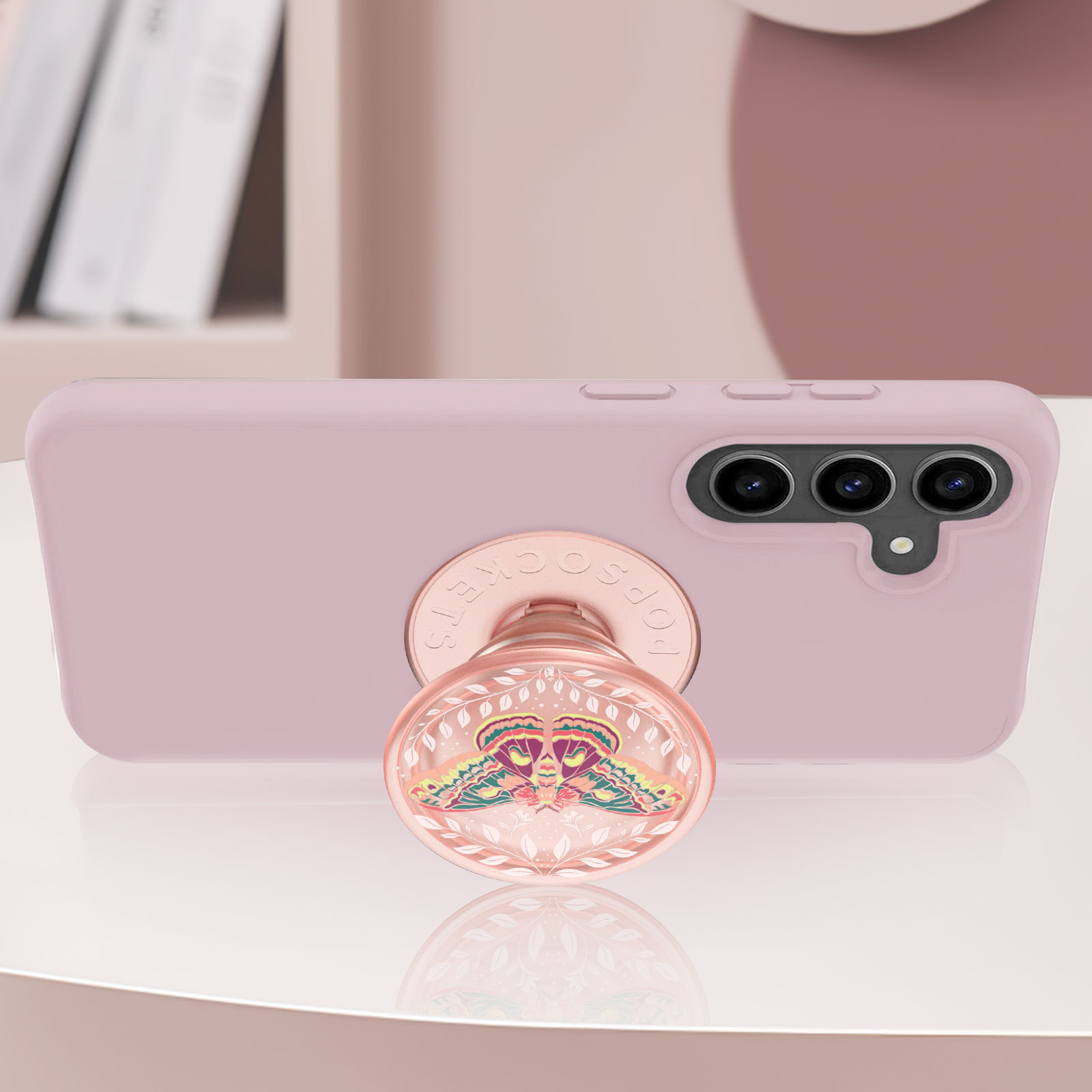 Telefono rosa con PopSocket a farfalla. Poggia su una superficie bianca.