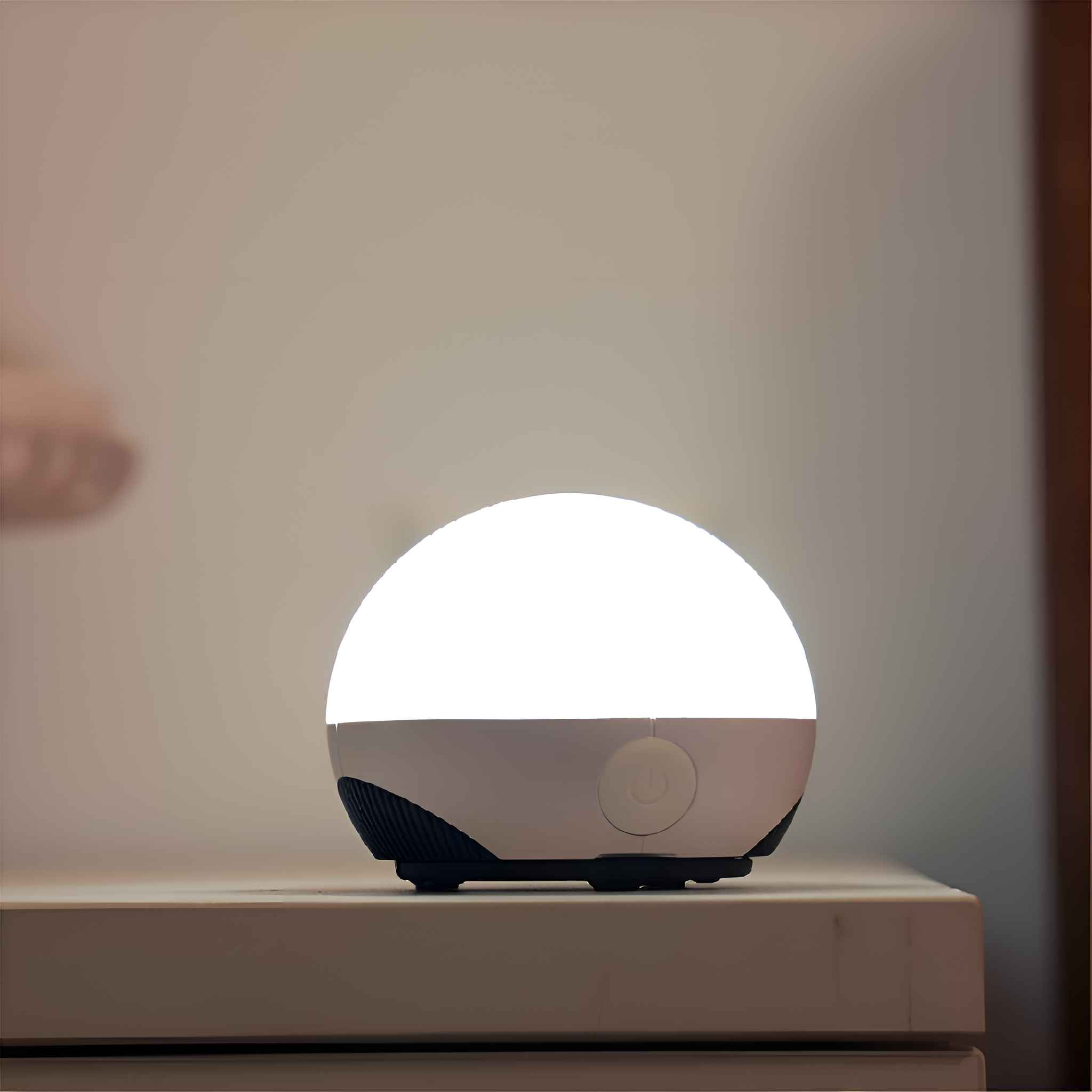 Eine runde, weiße Lampe mit hellem Licht. Sie steht auf einer hellen Oberfläche vor einer hellen Wand.