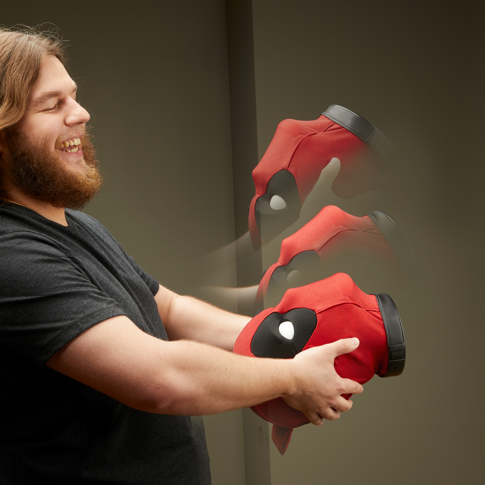 Adam Deadpool maskesi tutuyor, gülümsüyor. Kırmızı maske, siyah kenarlar, beyaz gözler. Hareket bulanıklığı.
