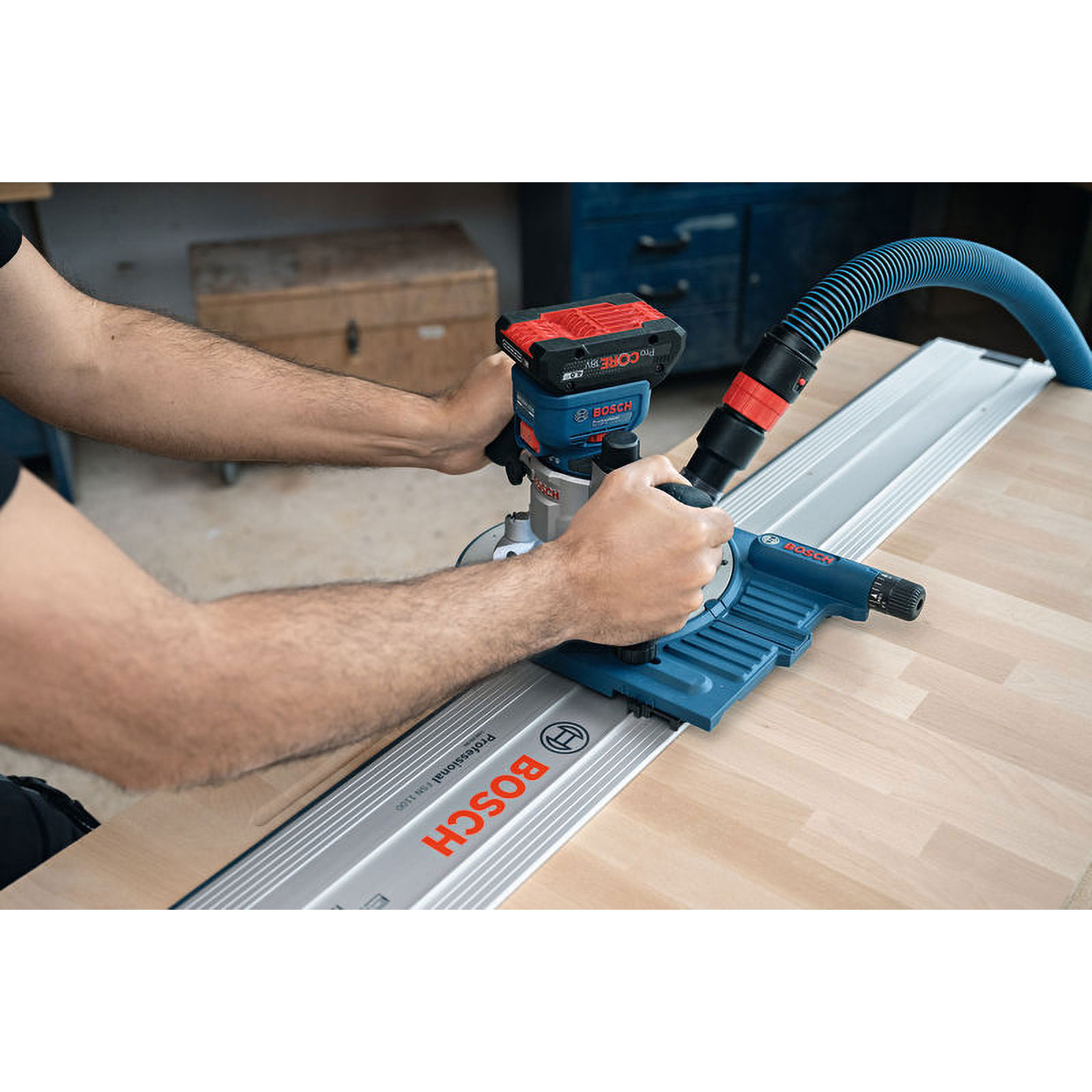 Eine Person benutzt ein Bosch-Werkzeug auf Holz. Das Werkzeug ist blau und silber mit einem roten Akku. Blauer Schlauch ist befestigt.