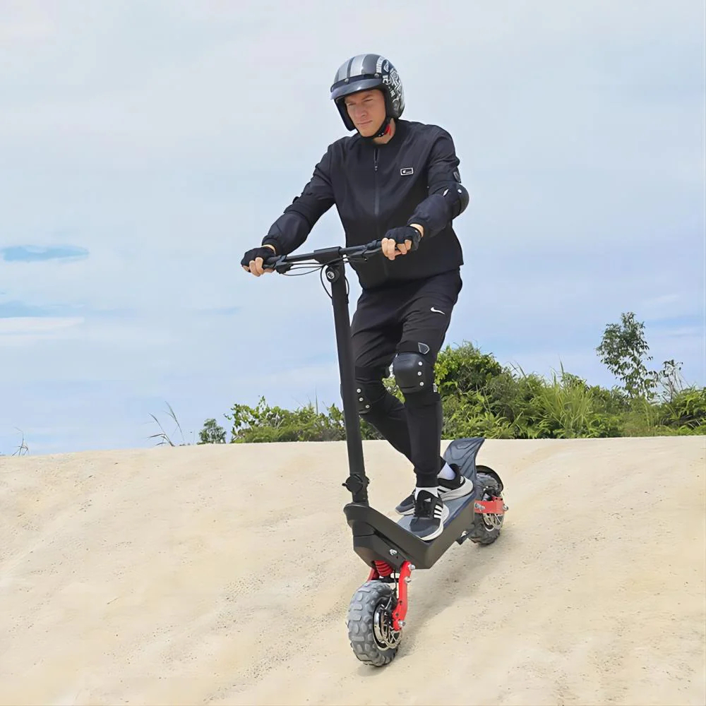 Osoba jedzie na hulajnodze elektrycznej po wydmie. Ma na sobie kask, czarne ubrania i sprzęt ochronny.