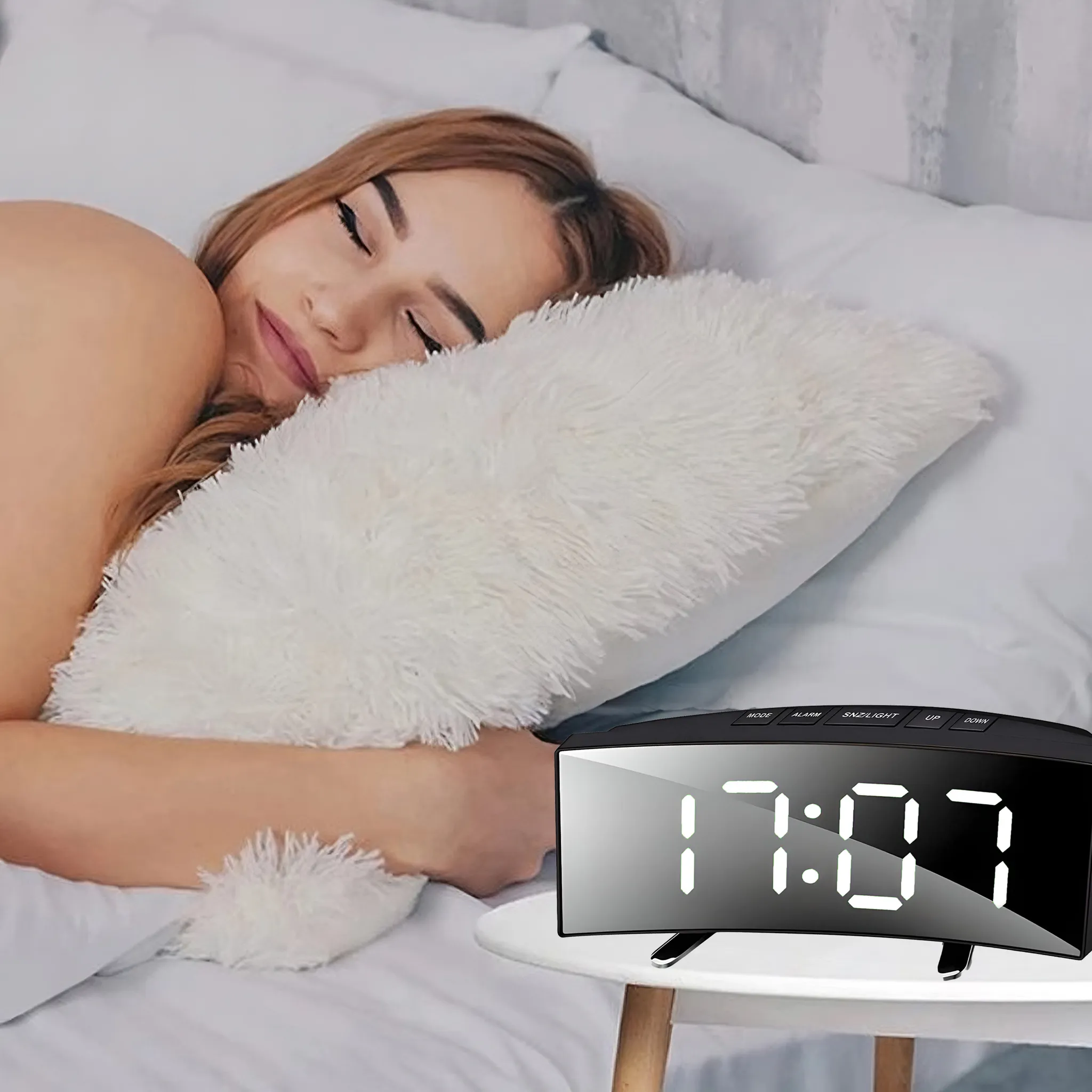 Eine Frau schläft im Bett mit einem weißen Kissen. Eine Digitaluhr zeigt 17:07 auf einem Nachttisch.