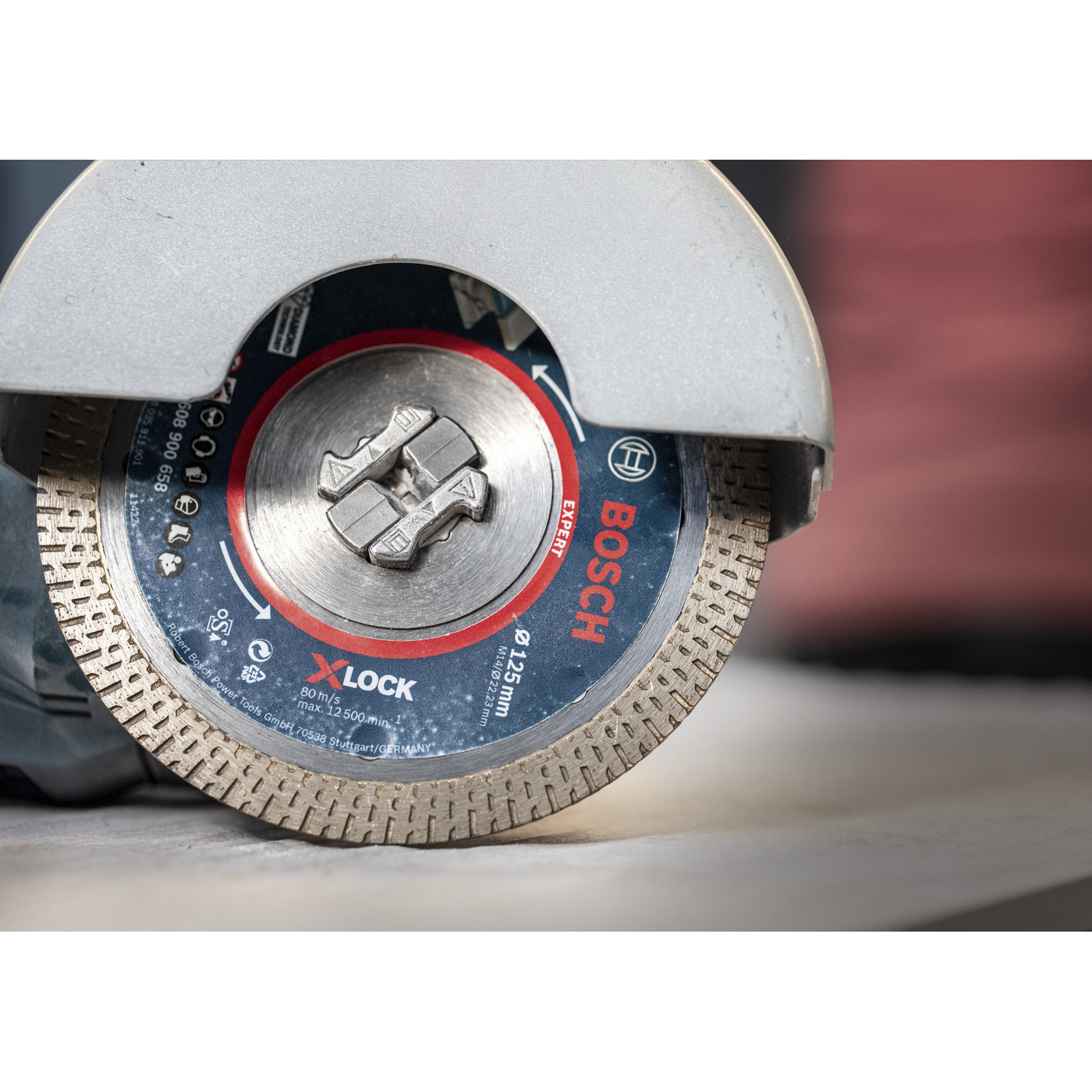 Nahaufnahme einer Bosch X-LOCK Trennscheibe. Sie ist an einem Schleifer mit Schutzhaube befestigt. Die Scheibe hat blaue und rote Details.