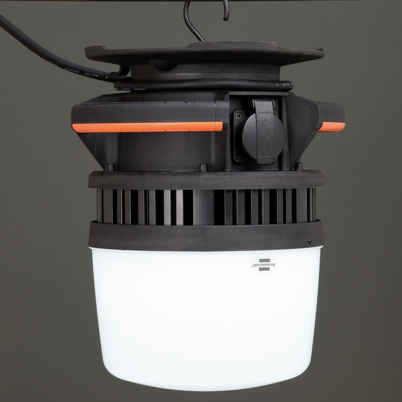 Eine schwarz-orange Arbeitsleuchte mit weißer Lampe, die an einem Haken hängt. An der Seite befindet sich eine Steckdose.