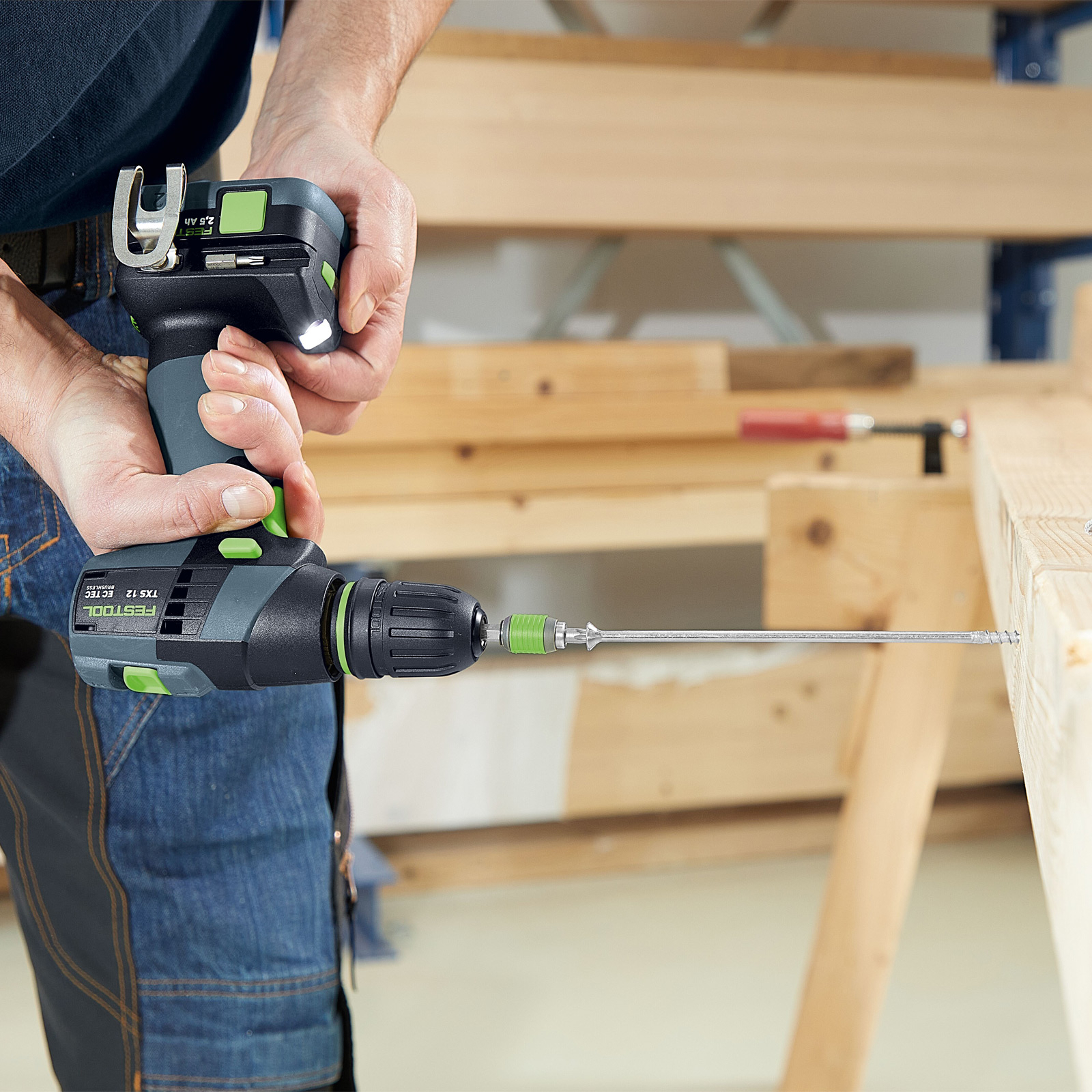 Una persona utiliza un taladro inalámbrico para atornillar en una viga de madera. El taladro es negro y verde.
