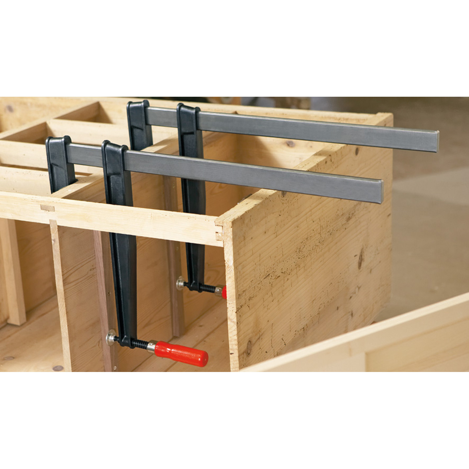 Drewniane pudełko montowane za pomocą zacisków. Dwa zaciski trzymają boki razem. Widoczne czerwone uchwyty.