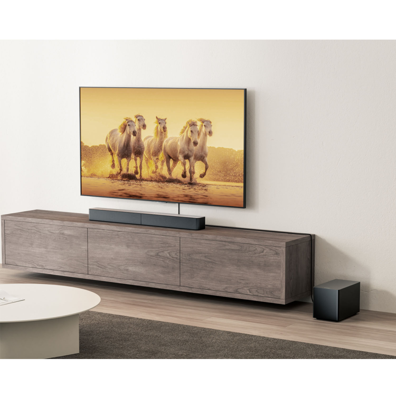 Ein Fernseher zeigt Pferde, die im Wasser laufen. Darunter befindet sich eine Soundbar auf einem Holzschrank. Ein Subwoofer ist rechts.