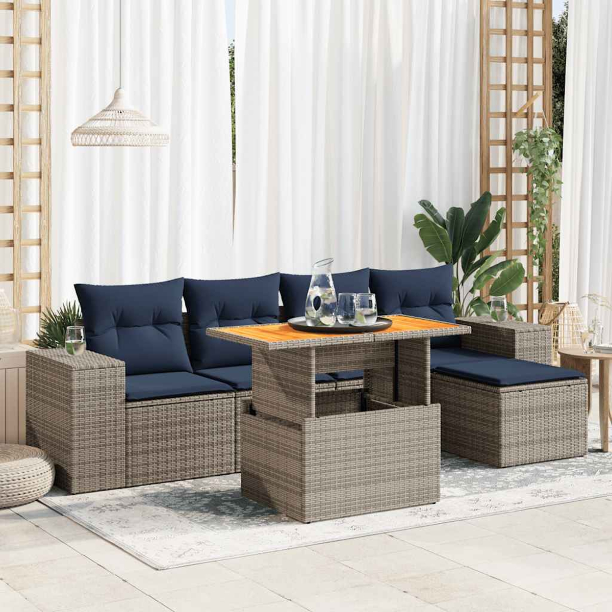 Outdoor-Terrassenset mit Sofa, Ottomane und Tisch mit Hubfunktion. Marineblaue Kissen, Rattanmöbel und weiße Vorhänge. Tisch hat eine Holzplatte.