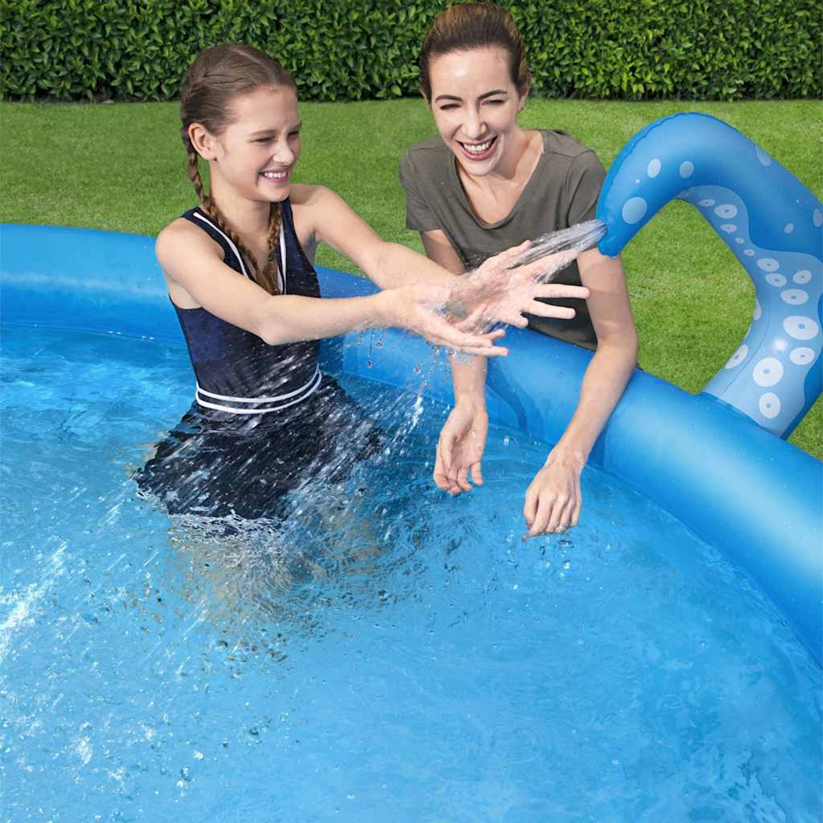 Zwei Frauen spielen in einem blauen Pool. Eine ist im Pool und spritzt mit Wasser. Ein aufblasbarer Oktopus spritzt Wasser.