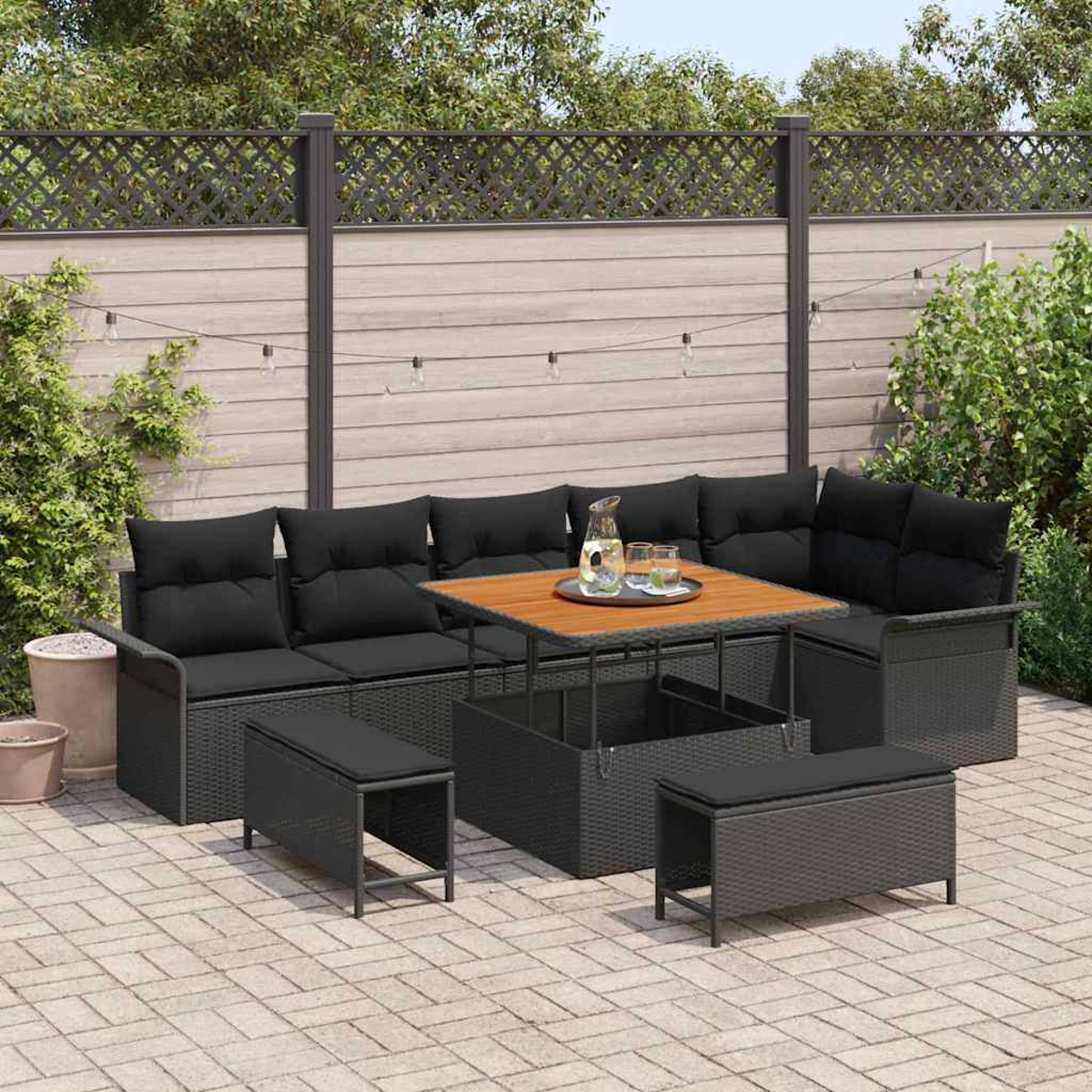 Garten-Sitzgruppe mit schwarzen Kissen und Holztisch. Enthält Bänke. Auf einer Backstein-Terrasse mit Zaun und Grün.