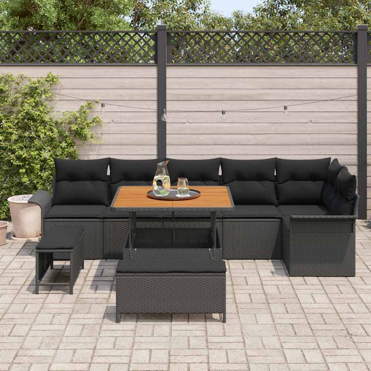 Outdoor-Terrassenset mit schwarzen Kissen und einem Holztisch. Enthält ein Sofa, eine Ottomane und eine Bank. Vor einem Holzzaun.