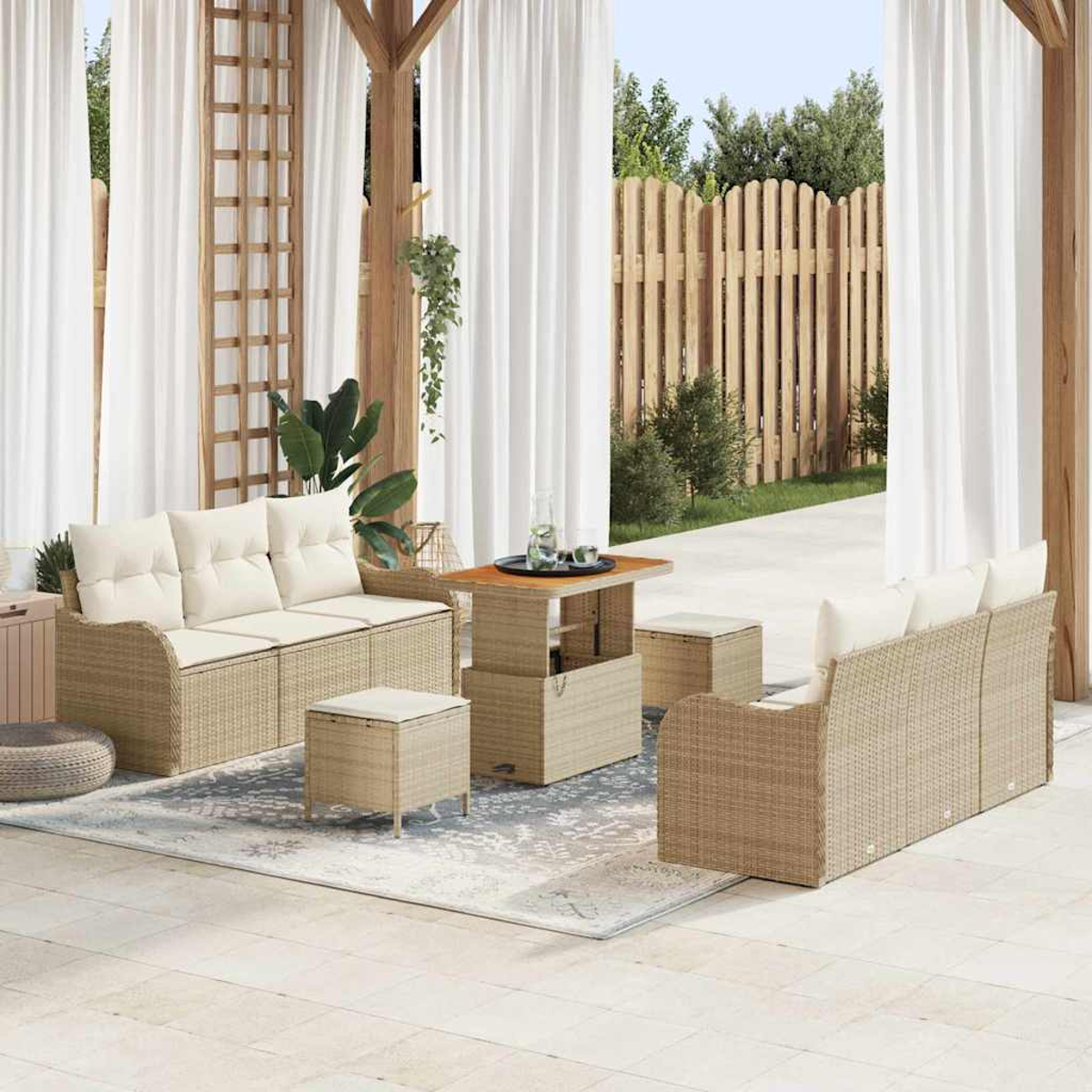 Terrassengarnitur mit Korbs Sofas, Ottomanen und Tisch. Weiße Vorhänge und Holzzaun im Hintergrund.