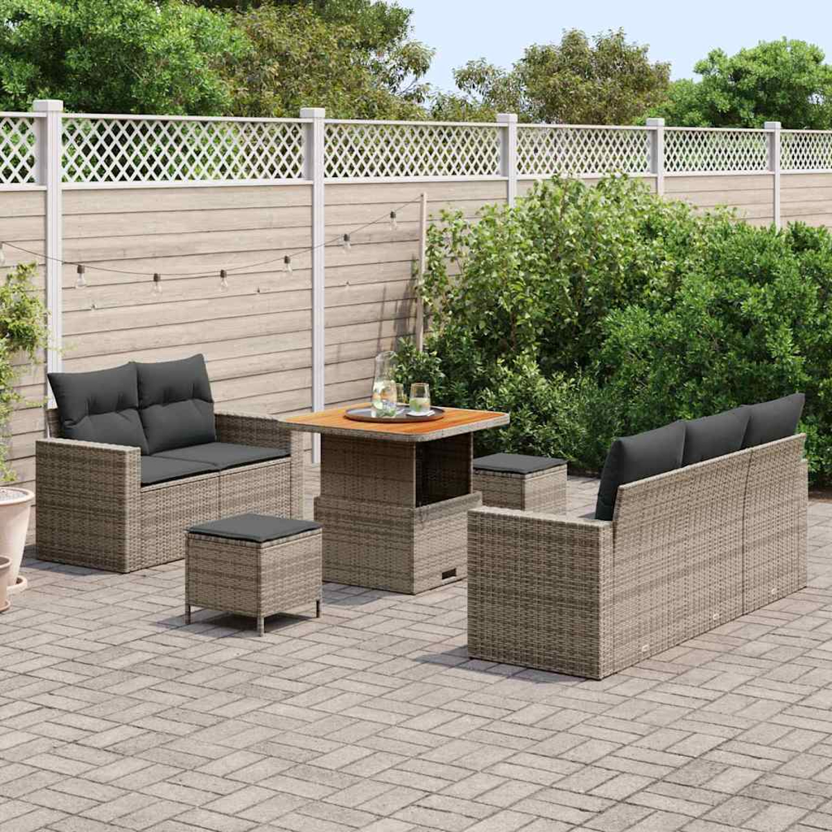 Garten-Terrassenset mit zwei Sofas, zwei Hockern und einem Tisch. Graue Kissen, braunes Korbgeflecht, auf einer Ziegelterrasse, mit weißem Zaun.
