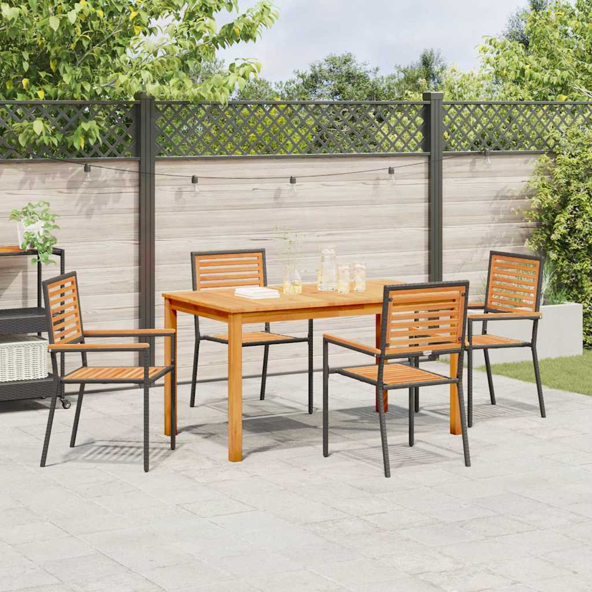 Essgruppe im Freien: Holztisch und Stühle auf einer Terrasse. Im Hintergrund ein Zaun und Grün. Lichterketten hängen darüber.