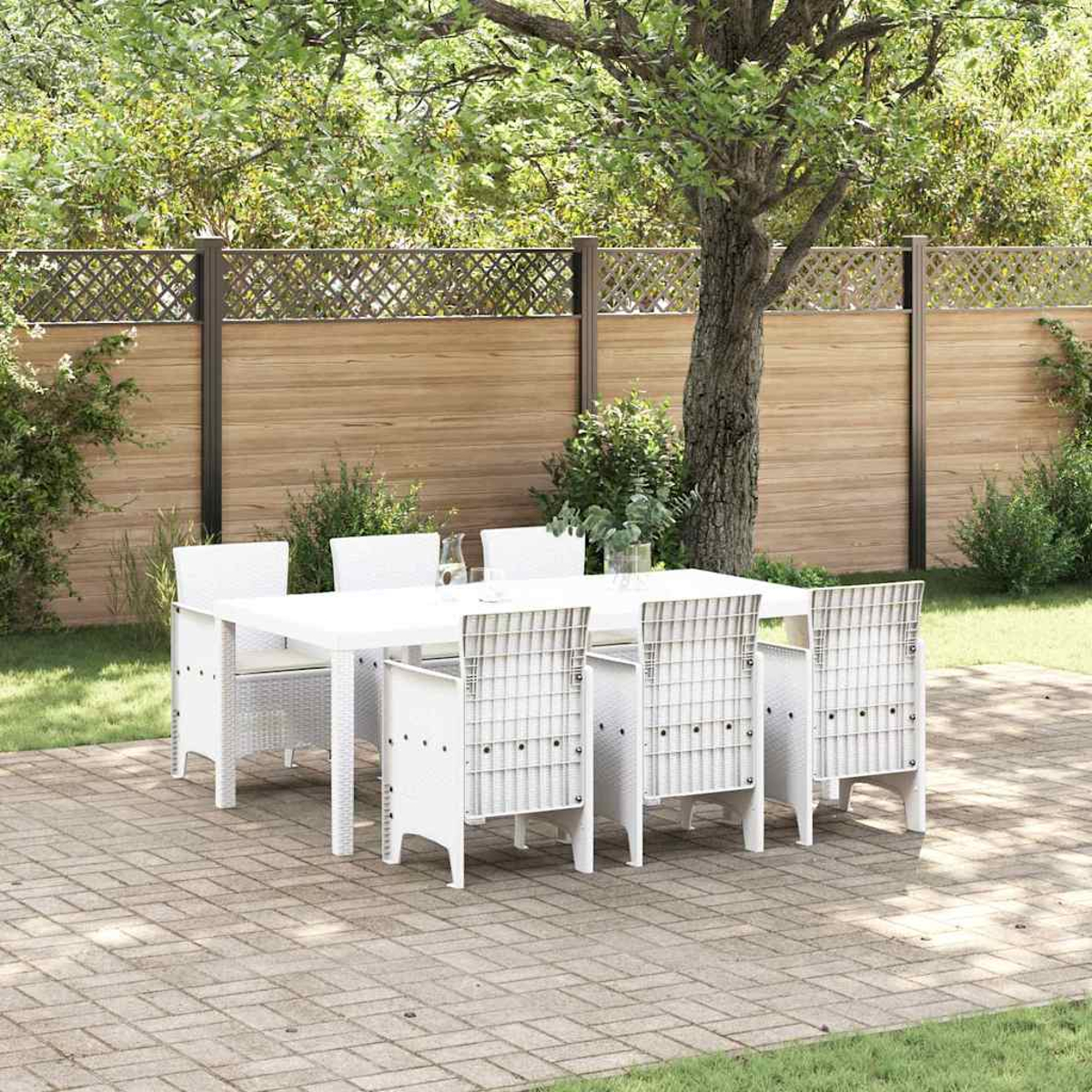 Weißes Esszimmerset im Freien auf einer Terrasse. Ein Tisch und Stühle stehen in einem Garten mit Holzzaun und Bäumen im Hintergrund.