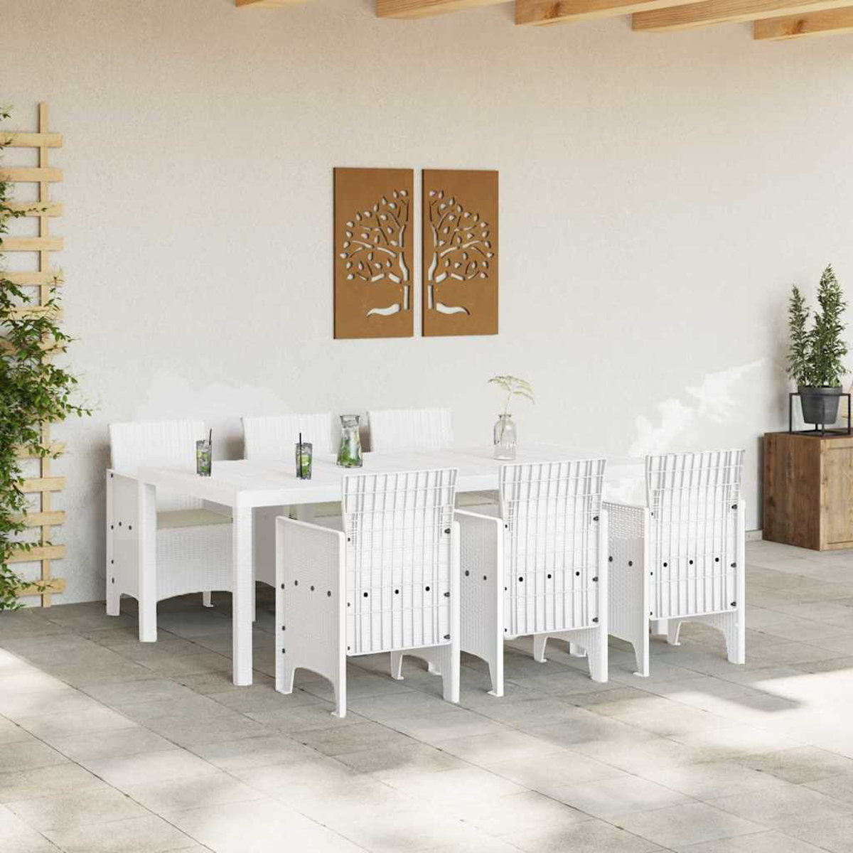 Weißes Ess-Set für den Außenbereich mit sechs Stühlen, einem Tisch und dekorativer Baumkunst an einer weißen Wand. Pflanzen und Holzakzente sind vorhanden.