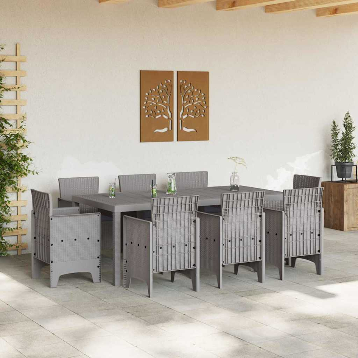 Ein Esszimmer-Set im Freien mit einem rechteckigen Tisch und acht grauen Stühlen. Zwei Baumkunstwerke hängen an der weißen Wand. Pflanzen sind an der Seite.