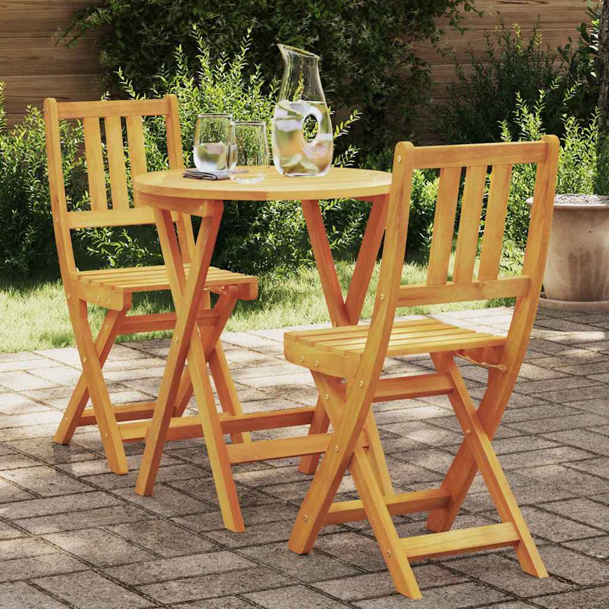 Holztisch und Stühle auf einer Terrasse. Eine Wasserkaraffe und Gläser stehen auf dem Tisch. Grünes Laub im Hintergrund.