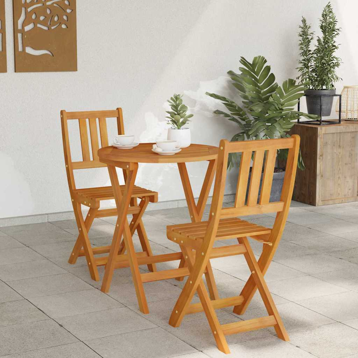 Holz-Bistrotisch-Set für den Außenbereich mit zwei Stühlen und einem runden Tisch. Auf dem Tisch stehen zwei Tassen und eine Pflanze. Der Hintergrund hat Pflanzen.