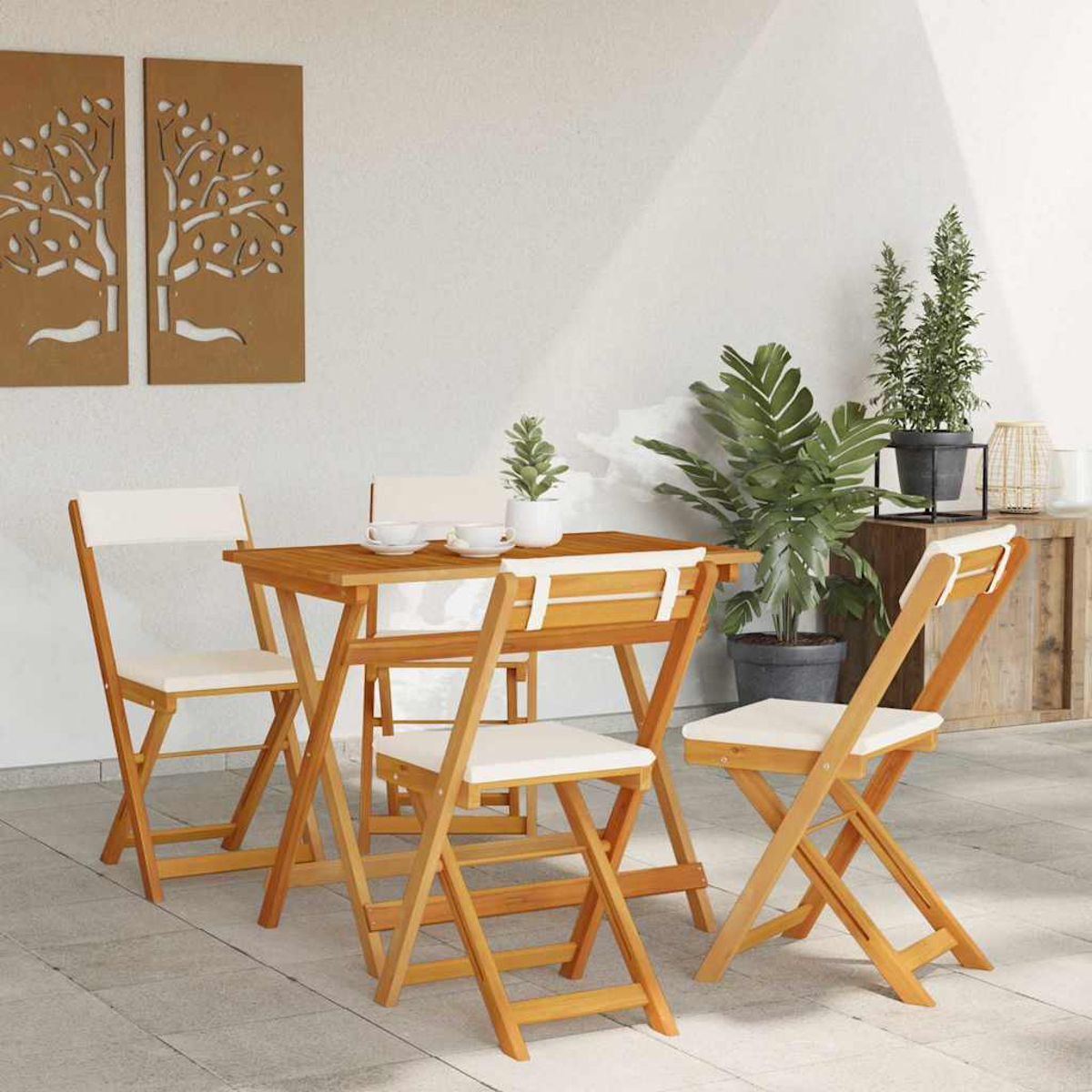 Holz-Terrassenset mit Tisch und Stühlen. Pflanzen in Töpfen und Wandkunst im Hintergrund. Weiße Kissen auf Stühlen.