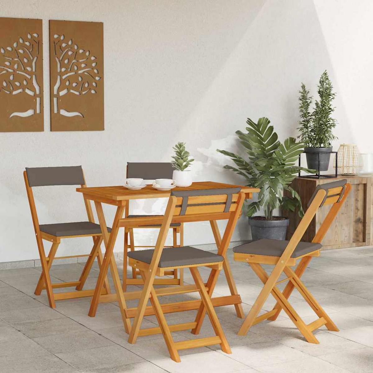 Essgruppe aus Holz im Freien mit vier Stühlen und einem kleinen Tisch. Pflanzen und dekorative Wandpaneele im Hintergrund.