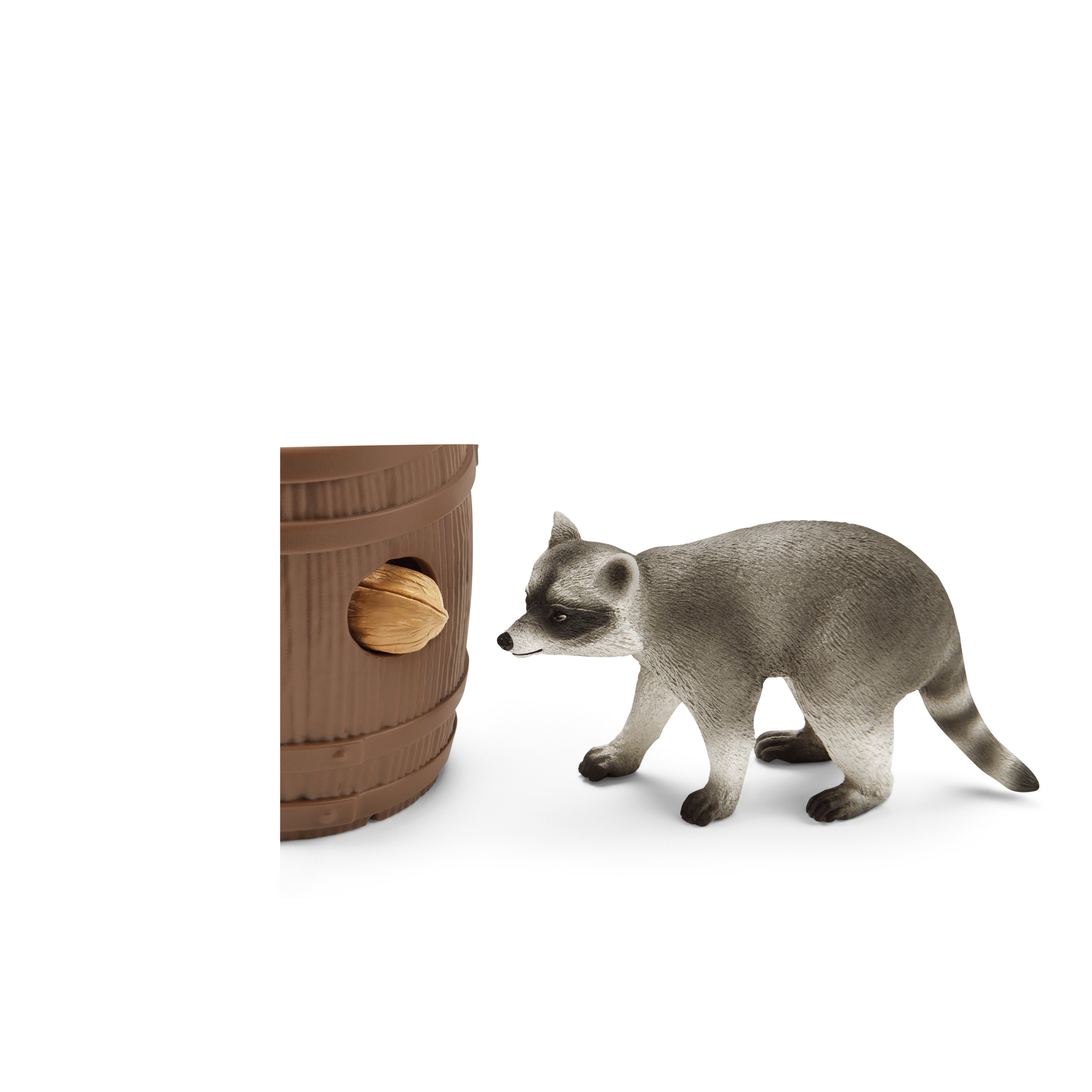 Ein Spielzeug-Waschbär steht neben einem braunen Fass mit einer Walnuss in der Öffnung, vor weißem Hintergrund.
