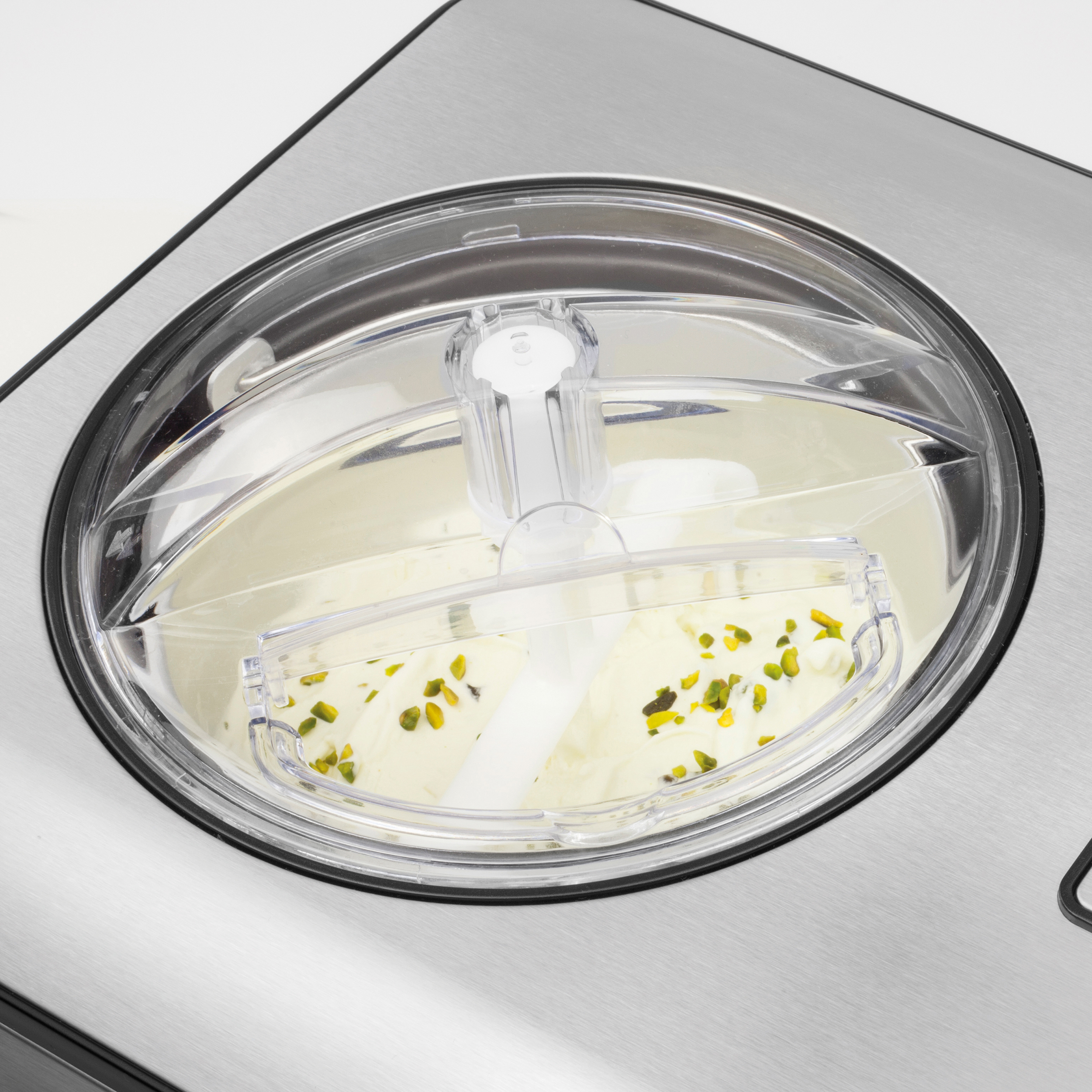 Eine Eismaschine mit einem transparenten Deckel. Die Maschine ist silberfarben, das Eis cremig mit grünen Pistazienstücken.