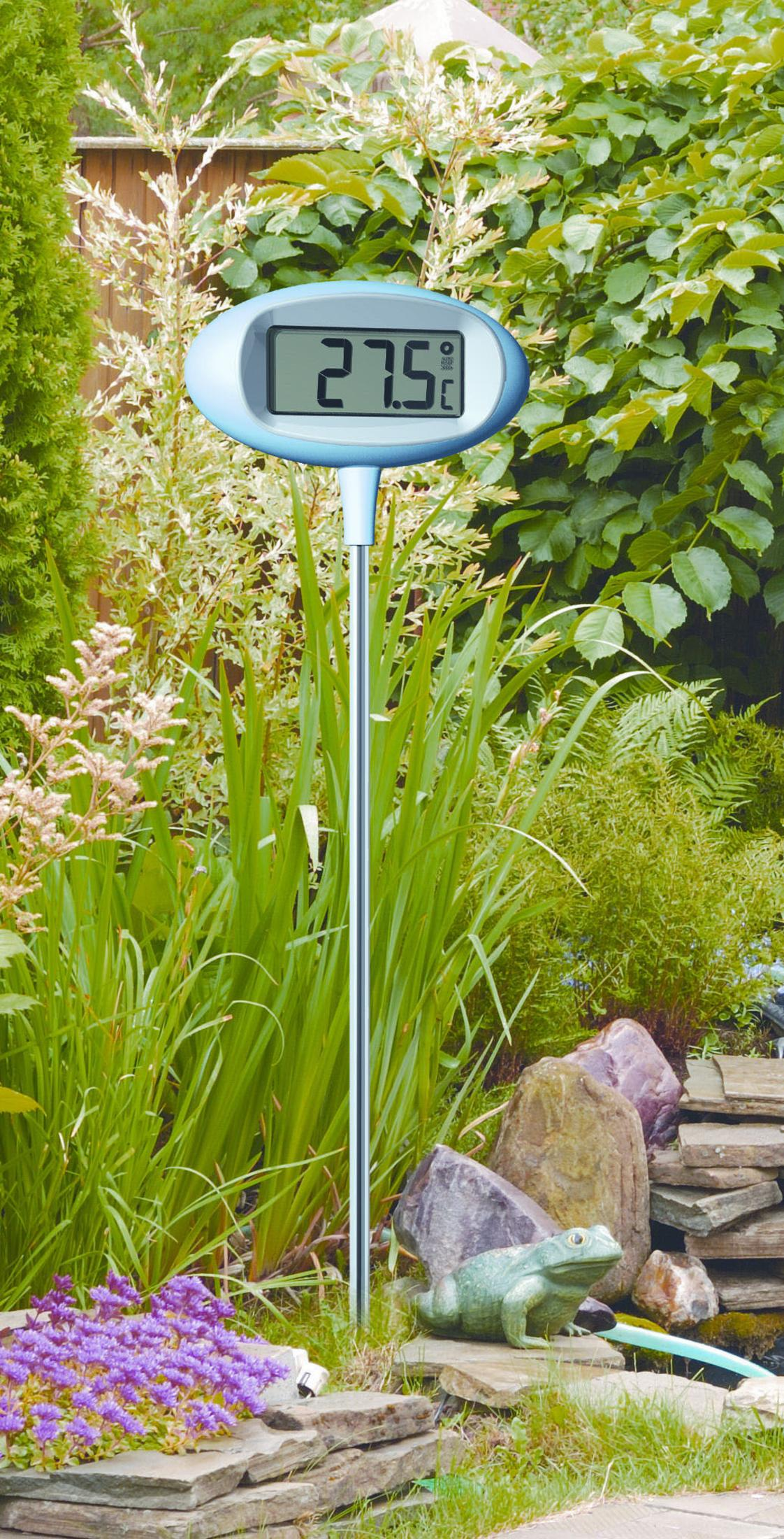 Eine Gartenszene mit einem Thermometer, das 27,5 °C anzeigt. Vordergrund: grüne Pflanzen und eine Froschstatue. Hintergrund: Büsche und ein Zaun.