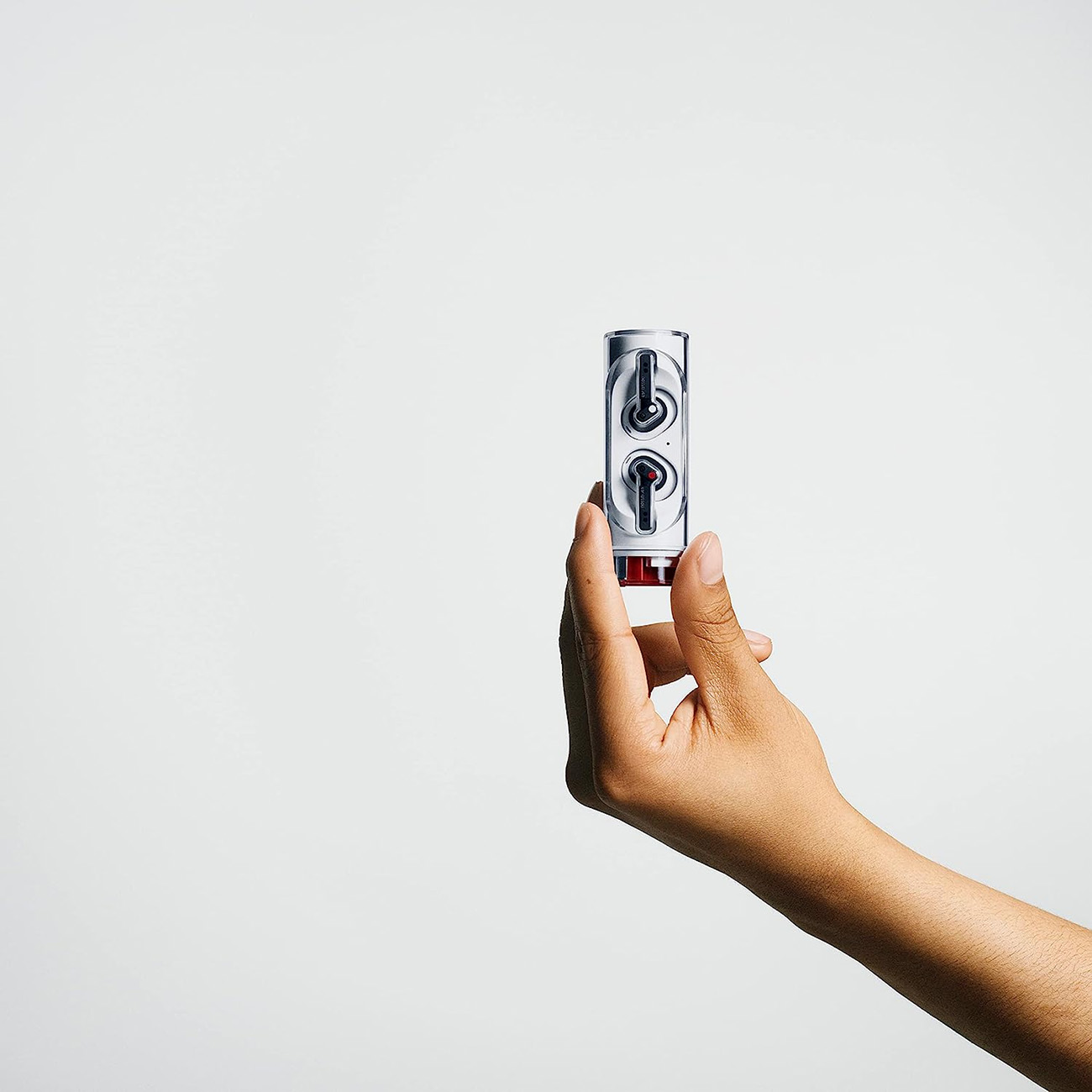 Una mano sostiene un estuche plateado y blanco para auriculares con dos auriculares dentro. El fondo es blanco liso.