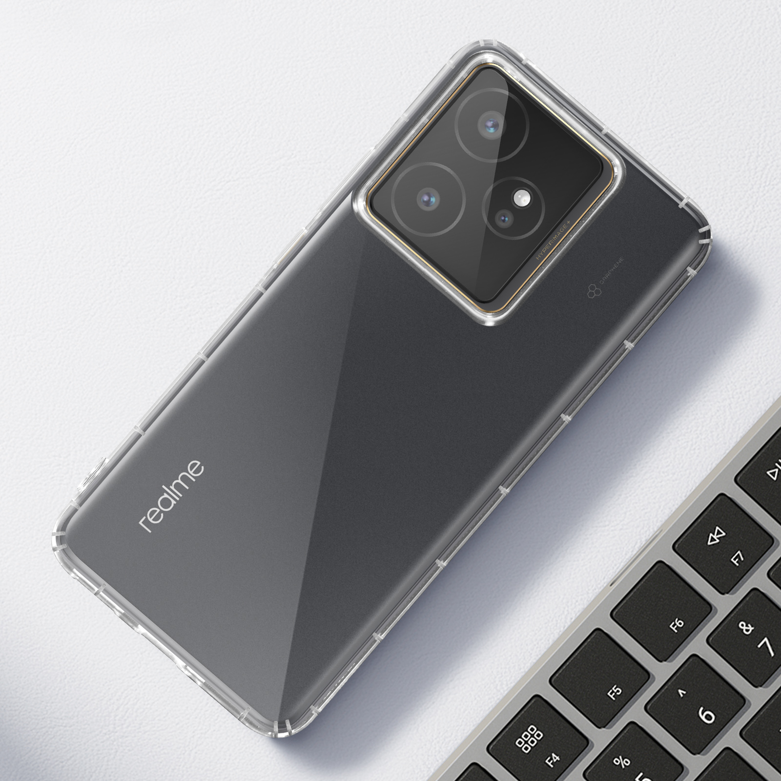Un téléphone dans un étui transparent repose sur une surface blanche. Un clavier est dans le coin. Le téléphone a trois caméras.