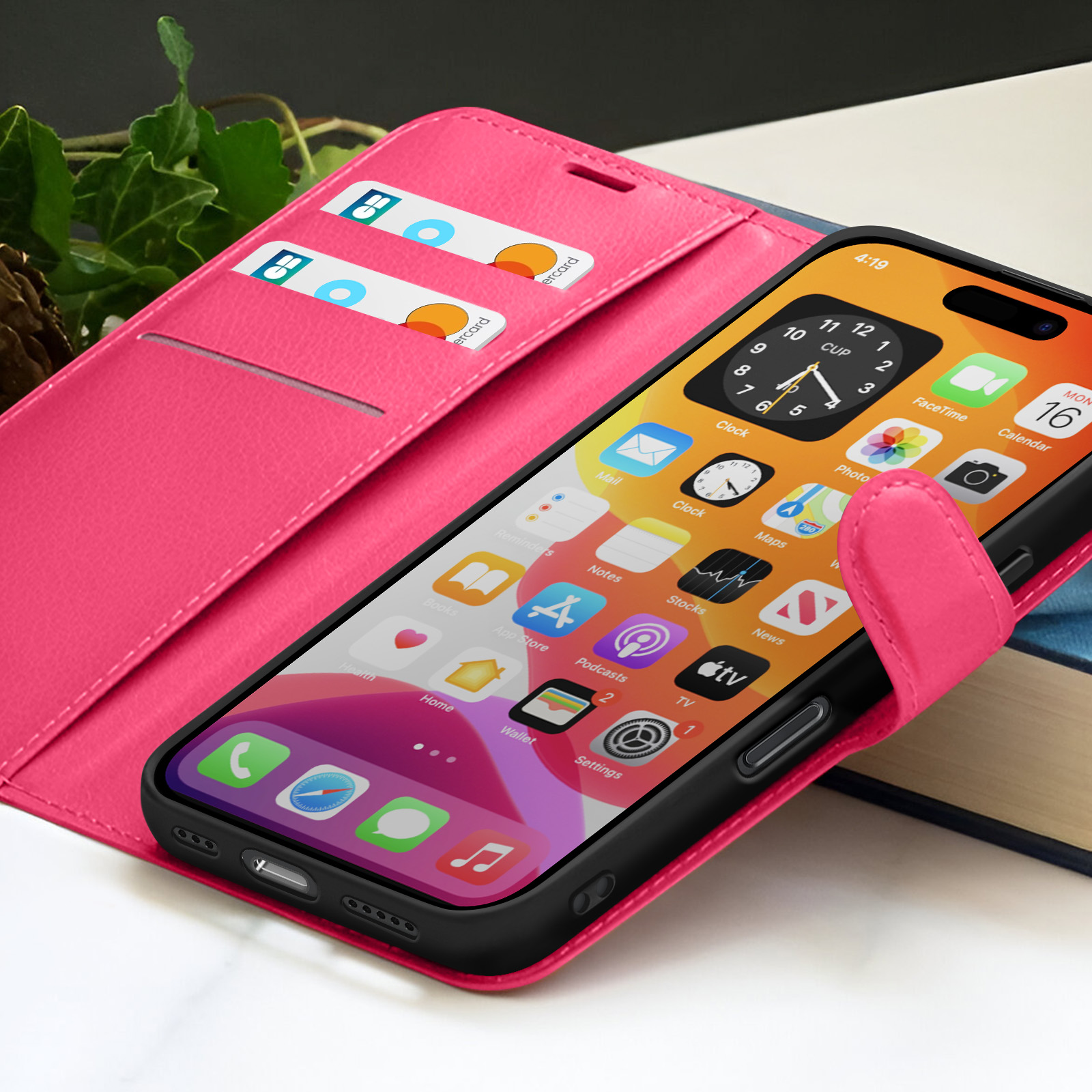 Un iPhone avec un étui noir dans un étui portefeuille rose avec des cartes de crédit. L'écran affiche diverses applications. Des feuilles de lierre en arrière-plan.