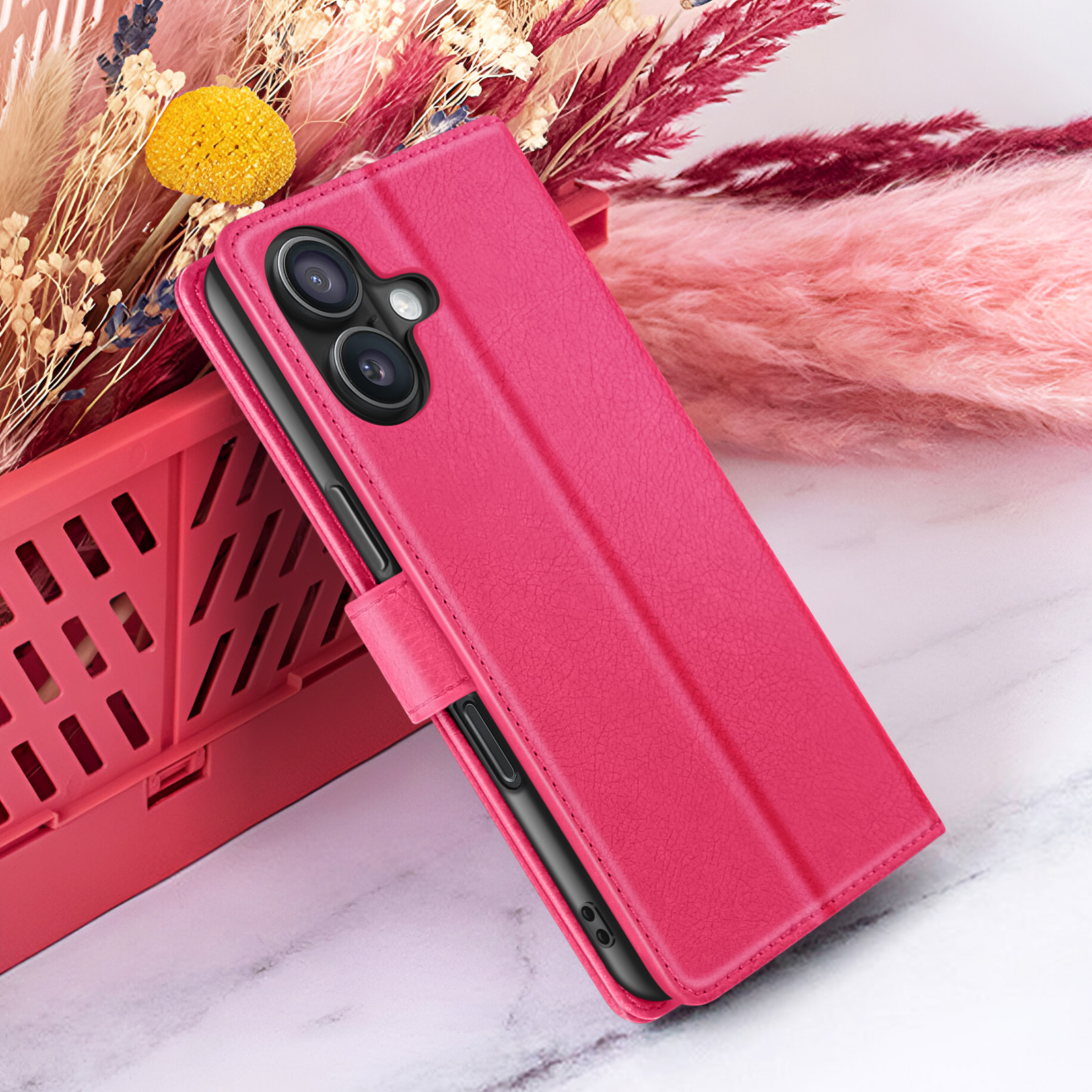 Étui de téléphone rose avec deux caméras, sur une boîte rouge avec des fleurs en arrière-plan. Surface effet marbre.
