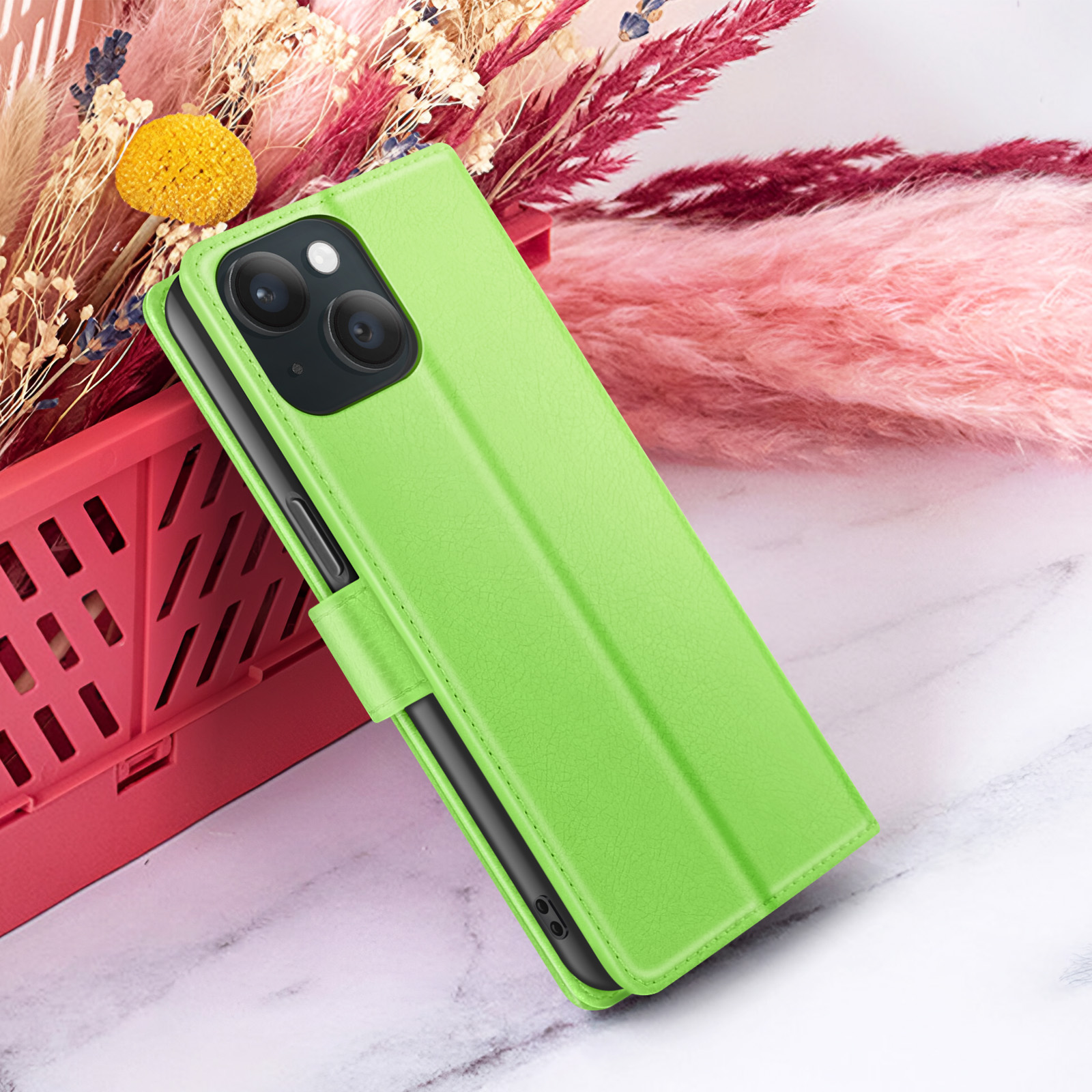 Un étui de téléphone vert citron avec un téléphone à l'intérieur, placé sur une surface en marbre. Fond : fleurs et un panier rouge.