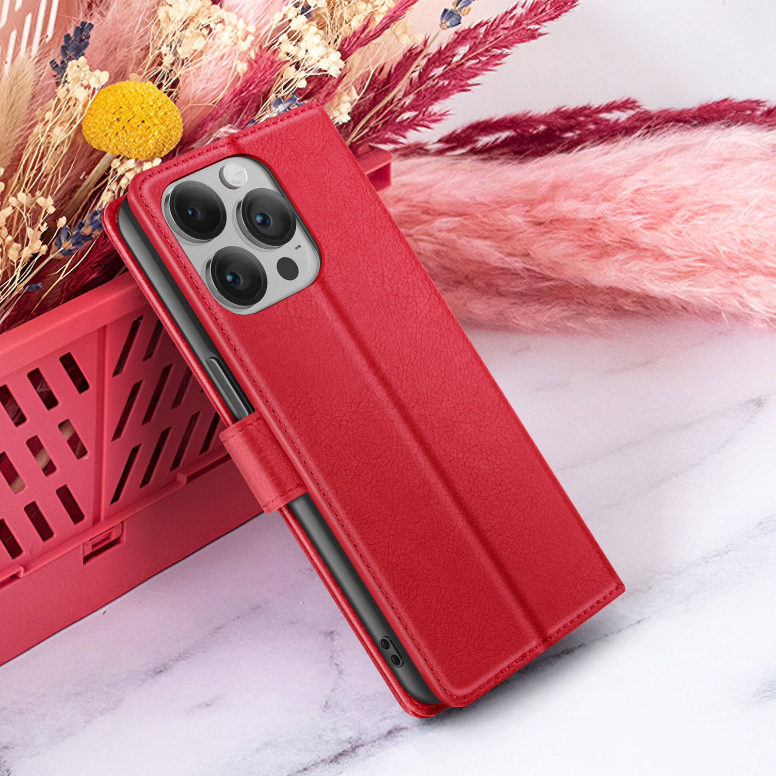 Een rode telefoonhoes met een telefoon erin ligt op een marmeren oppervlak. Gedroogde bloemen in roze en geel staan op de achtergrond.