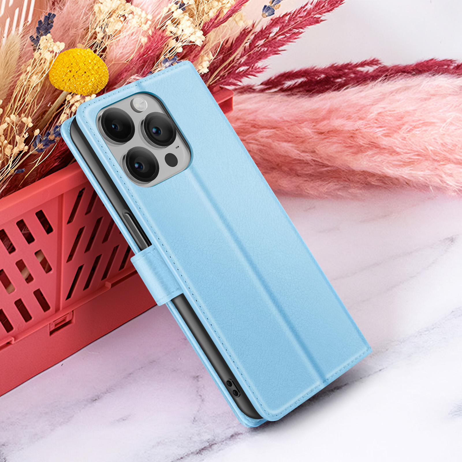 Un étui de téléphone bleu avec un téléphone à l'intérieur, placé sur une surface en marbre, avec des fleurs en arrière-plan.