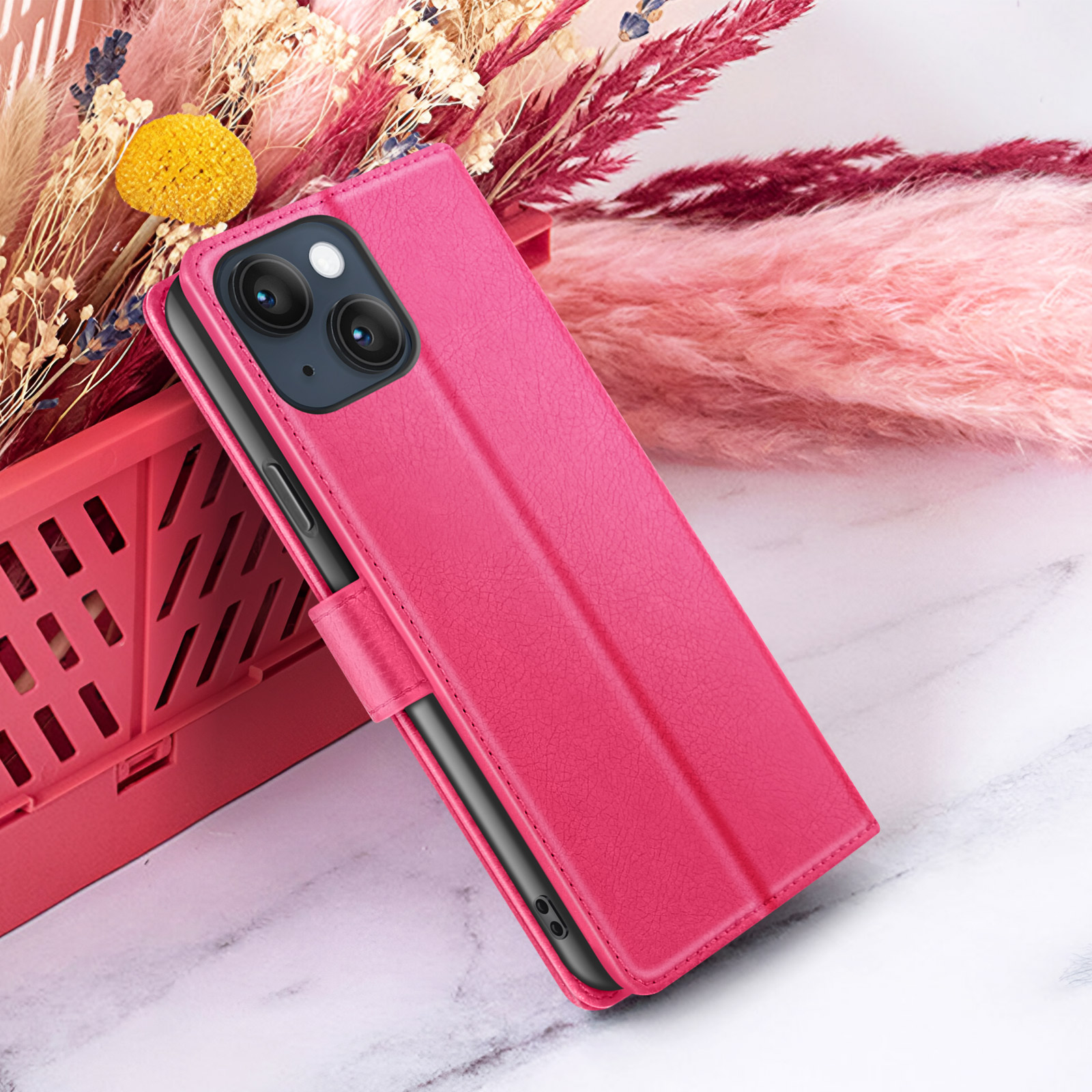Un étui de téléphone rose avec un téléphone à l'intérieur, sur fond de fleurs séchées et de surface rose.
