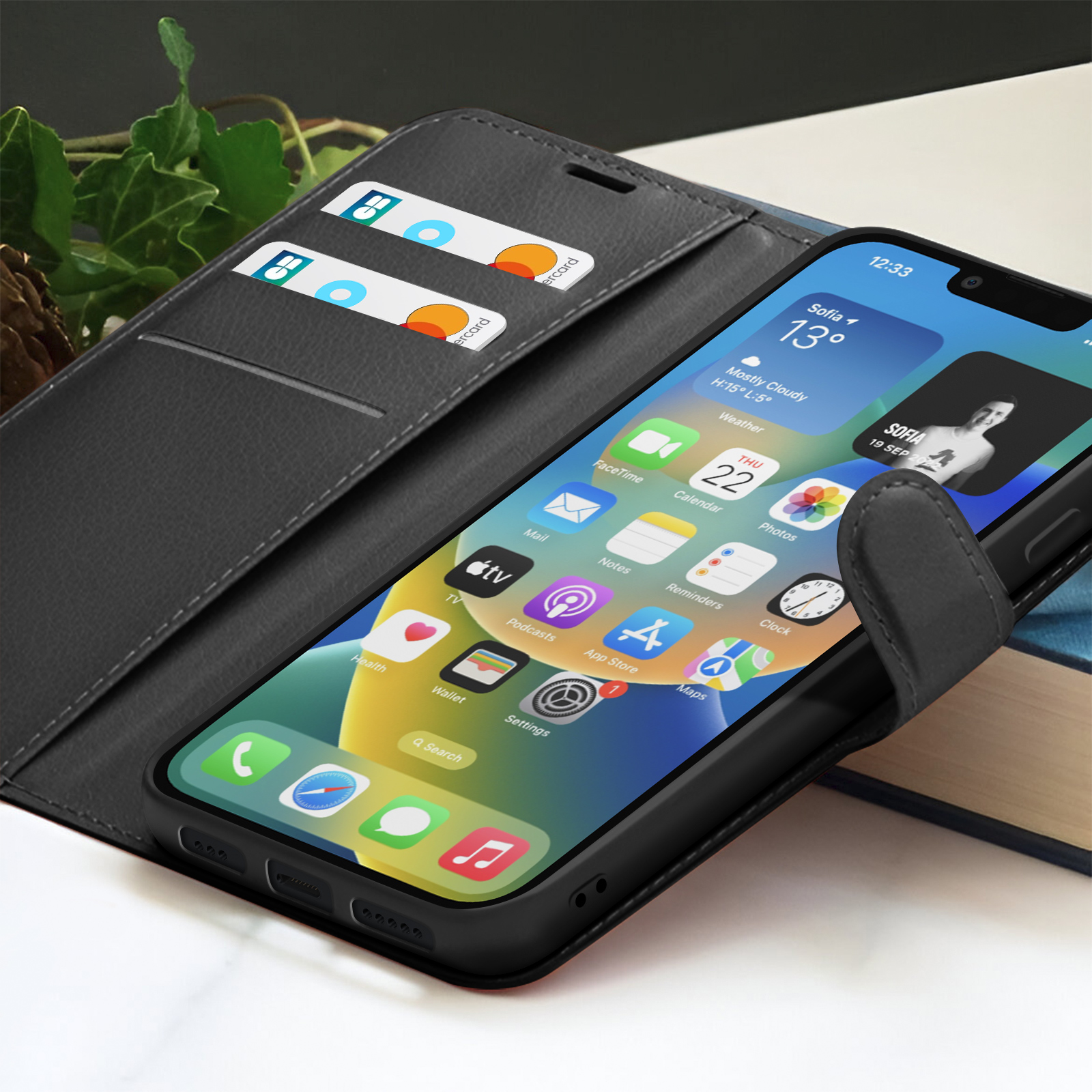 Téléphone noir dans un étui avec cartes de crédit. L'écran affiche l'application météo et d'autres icônes. Feuilles vertes en arrière-plan.